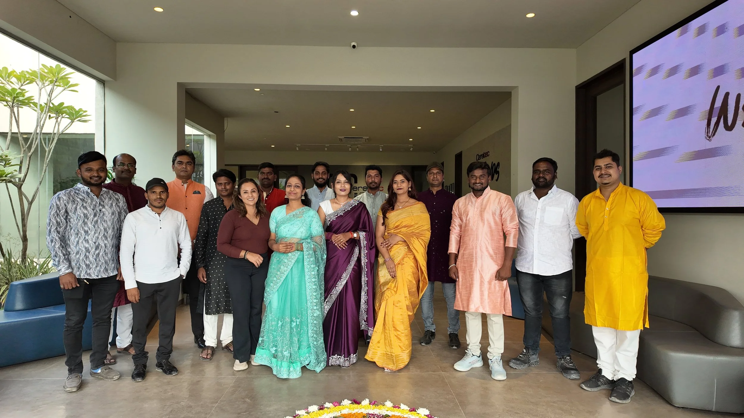 Group of men and women standing inside a modern building, some wearing traditional Indian clothing, posing for a photo.