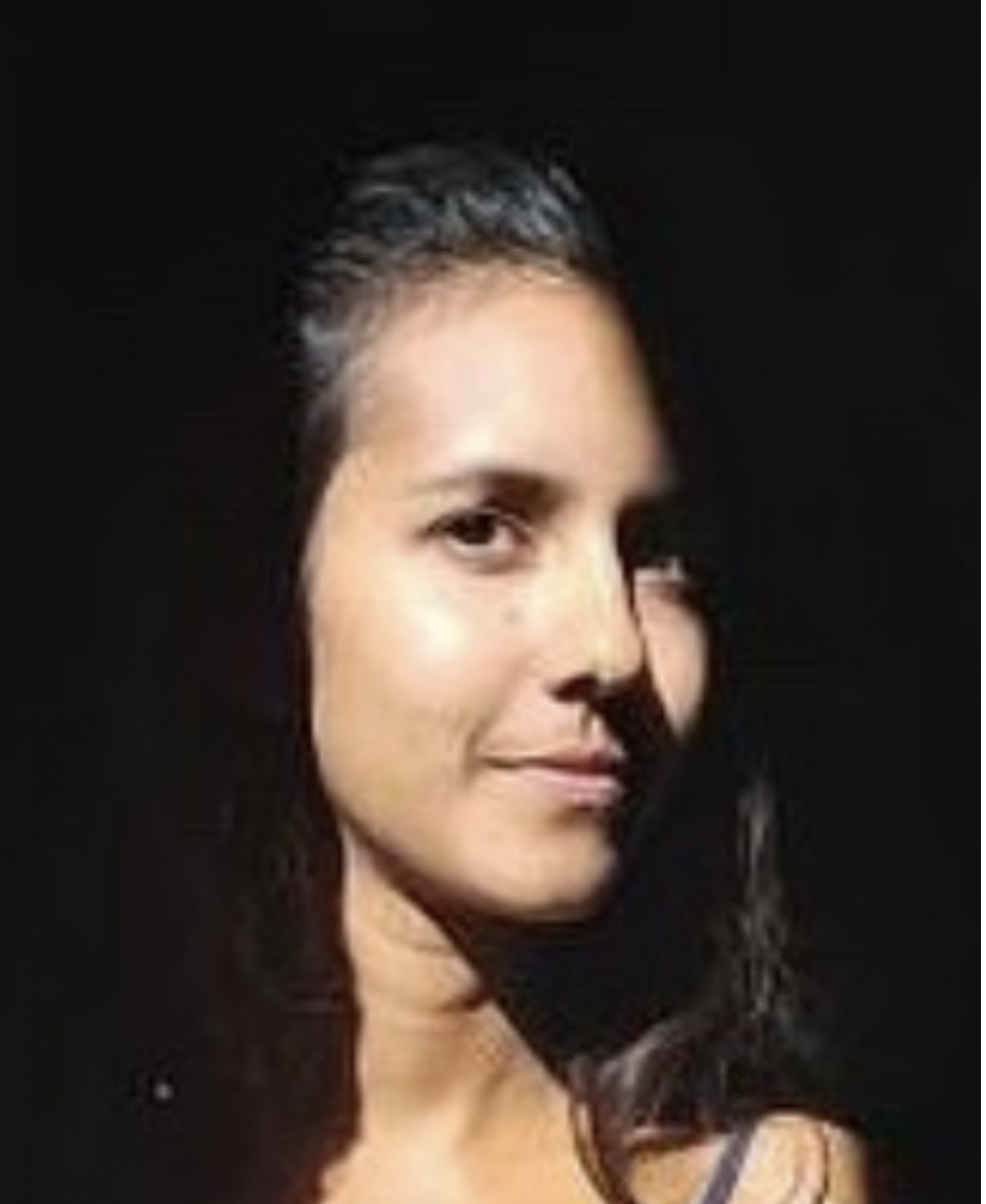 Retrato de una mujer con cabello oscuro y rizado, con piel clara y expresión confiada, en un fondo negro.