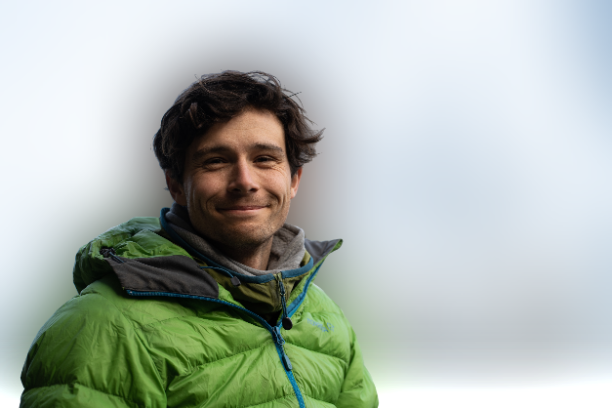 Man in a green jacket smiling outdoors against a cloudy sky