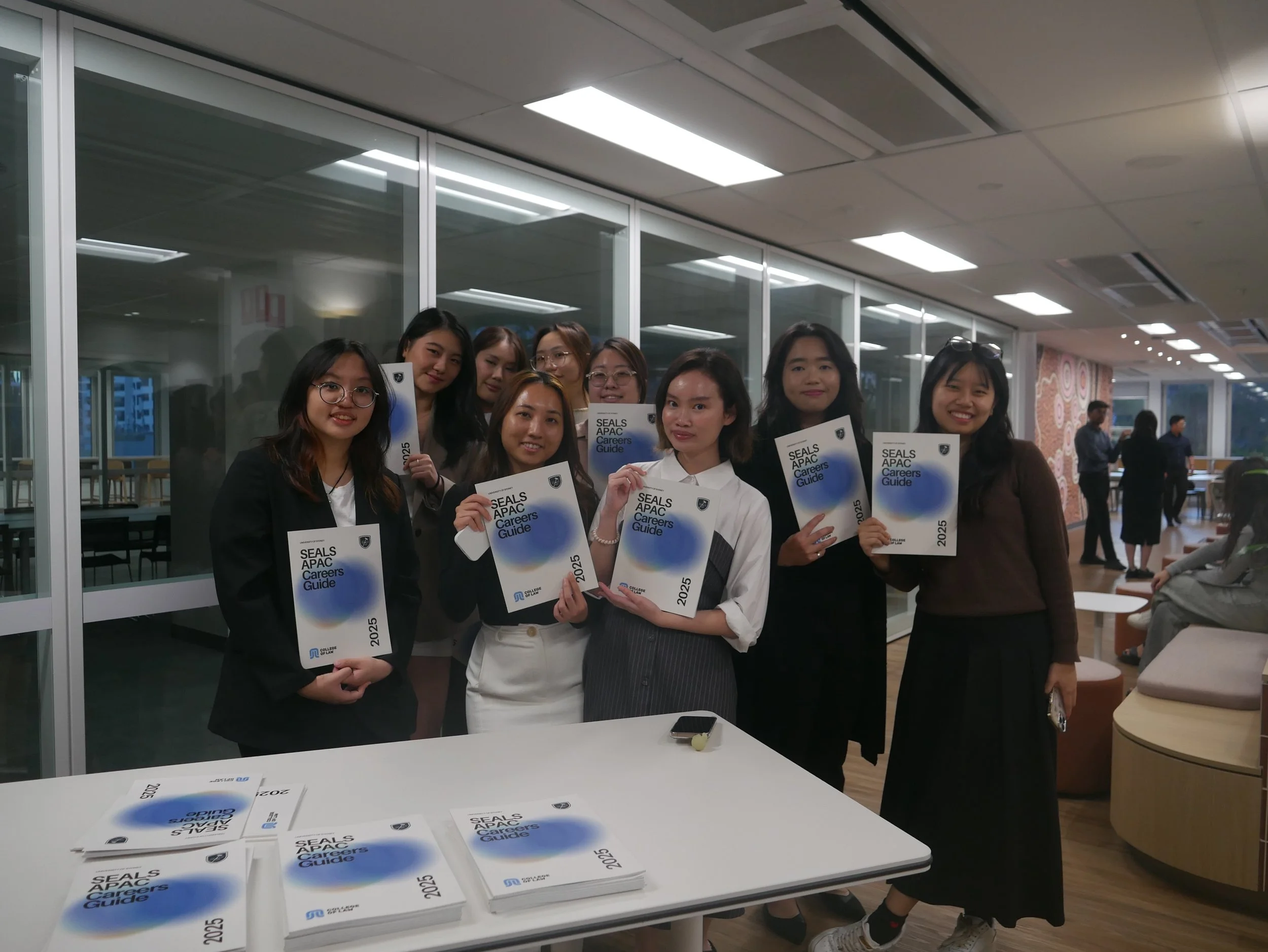 Group of eight women standing in an office, holding copies of the SEALS APAC Careers Guide 2025, smiling at the camera.