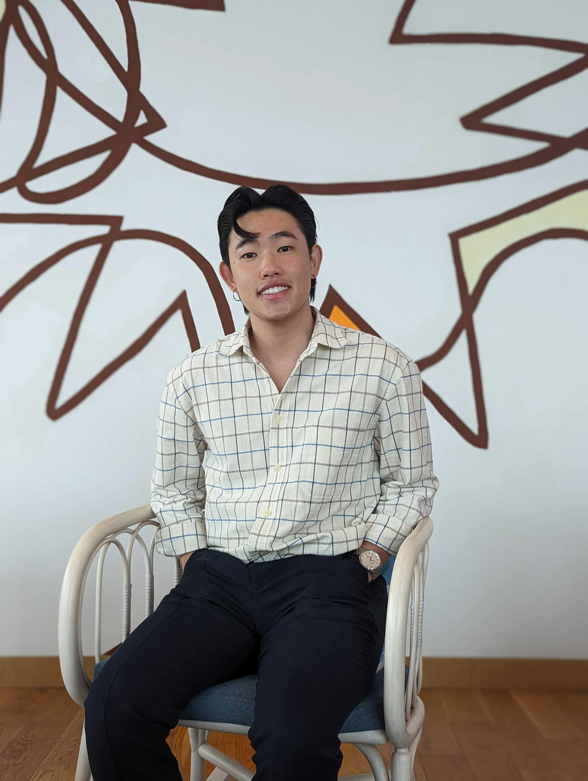 A young man sitting on a chair with a modern, abstract wall art behind him.