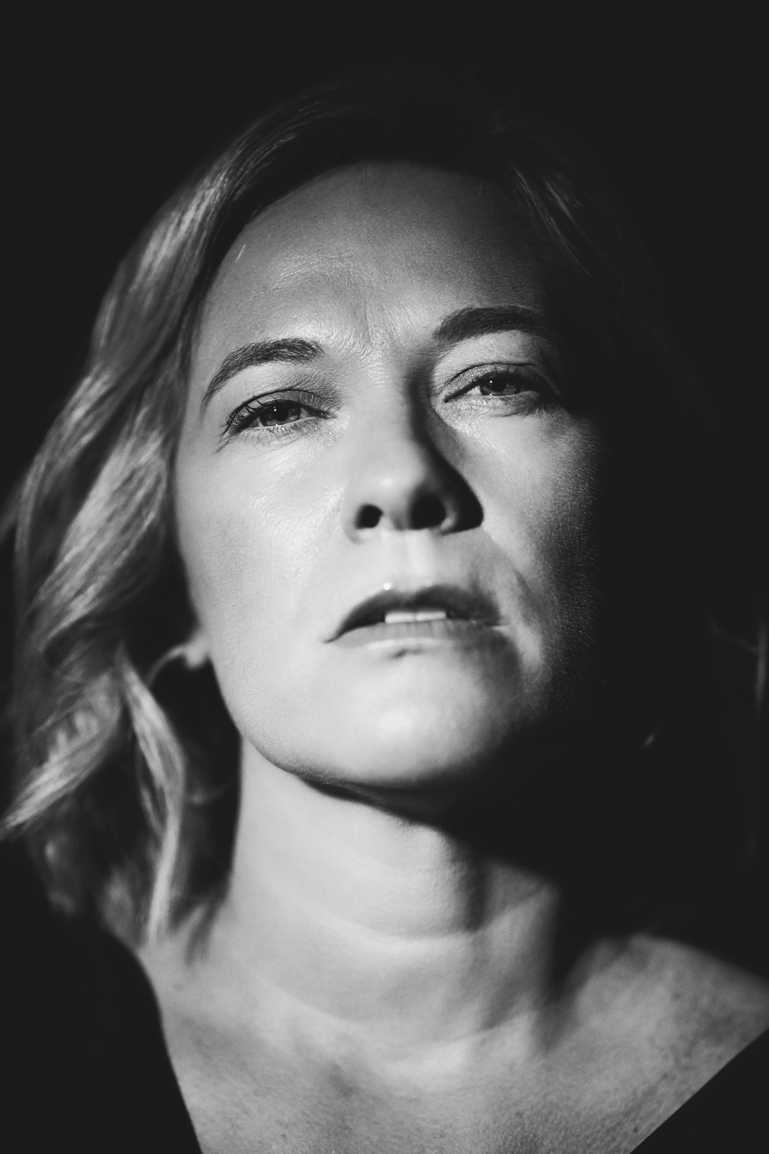 A close-up black-and-white portrait of a woman's face, showing her eyes, nose, and lips with wavy hair on the side.