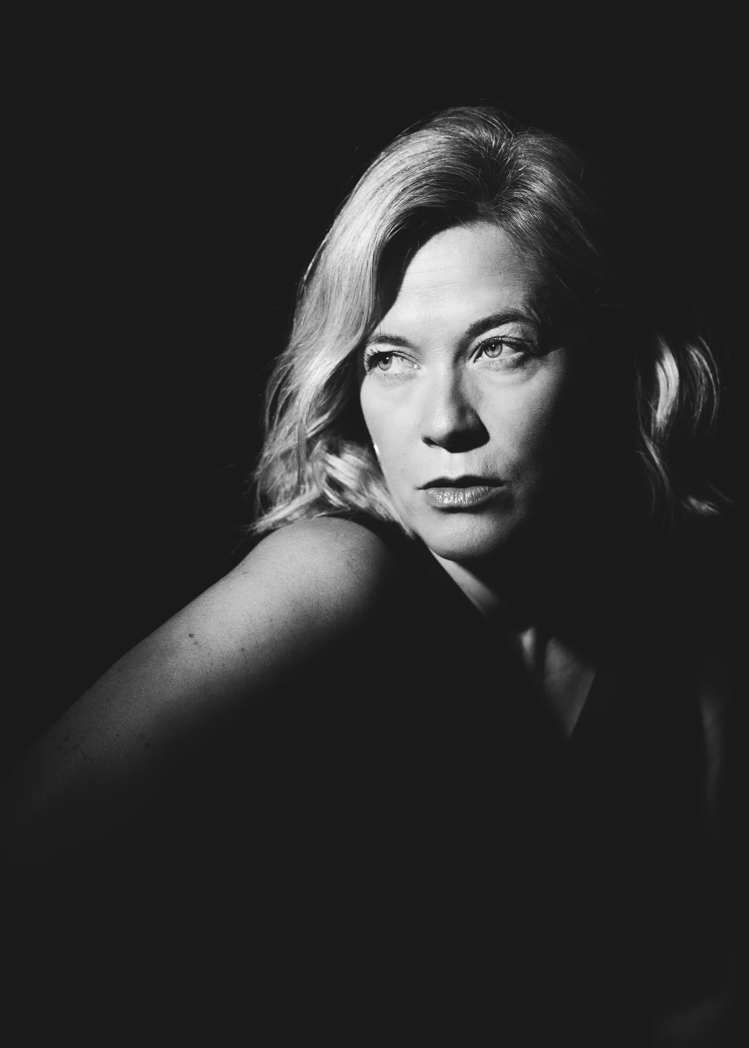 Black and white portrait of a woman with wavy hair looking to the side against a dark background.