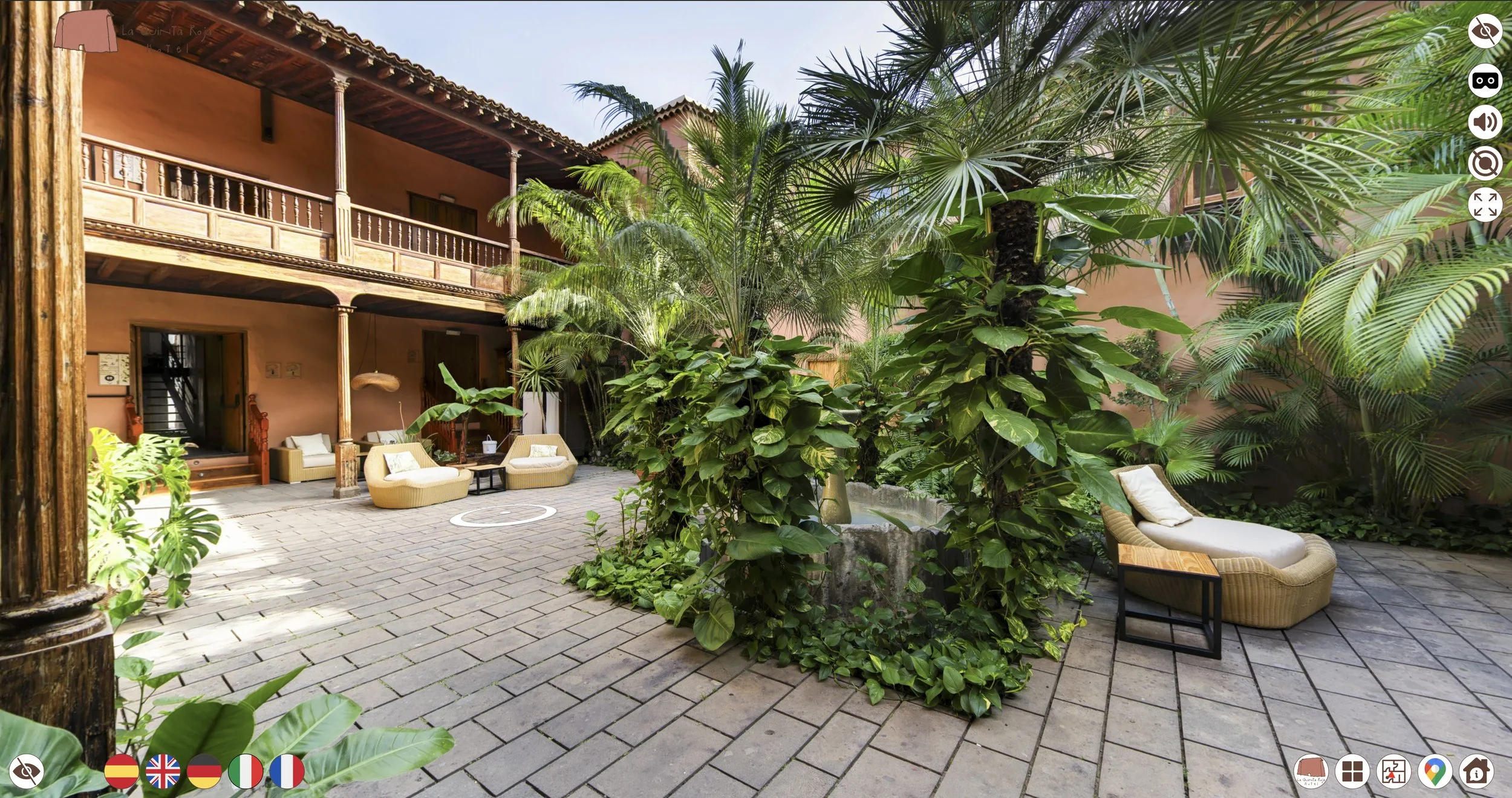Courtyard with lush tropical plants, outdoor seating including wicker chairs and loungers, and two-story building with balcony and wooden columns.