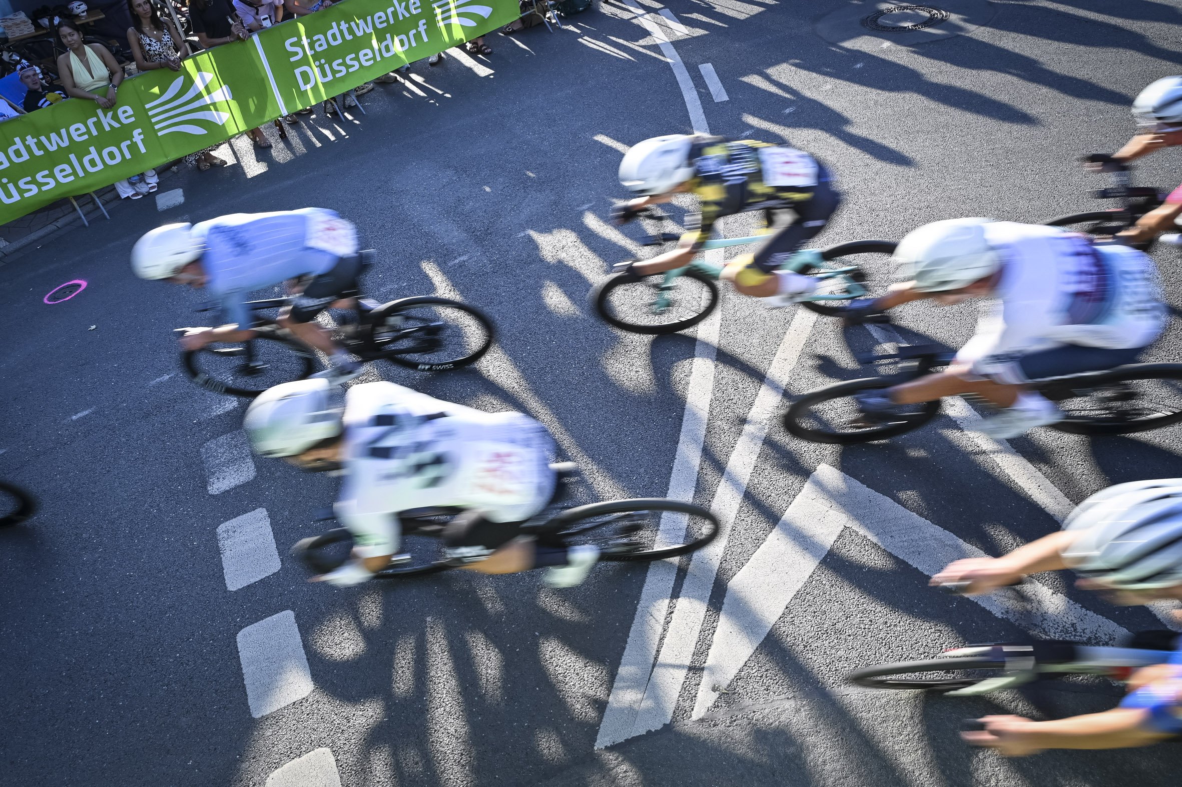 Radfahrer bei einem Rennen, schnelle Bewegung, auf einer städtischen Straße mit Zuschauern im Hintergrund, Banner mit 'Stadtwerke Düsseldorf'.