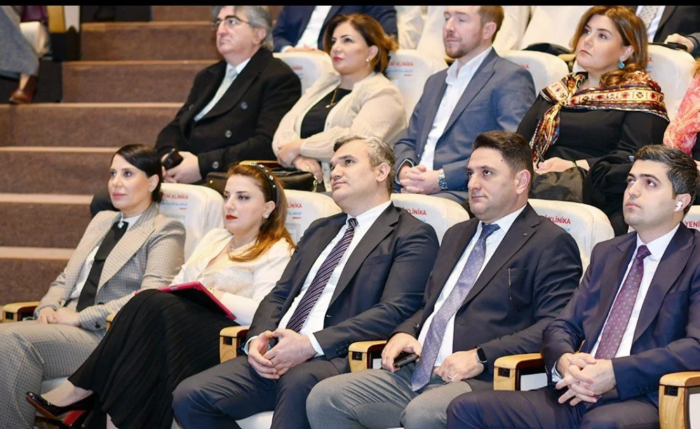 Group of professionally dressed people sitting in an auditorium, attentively listening to a presentation or speech.