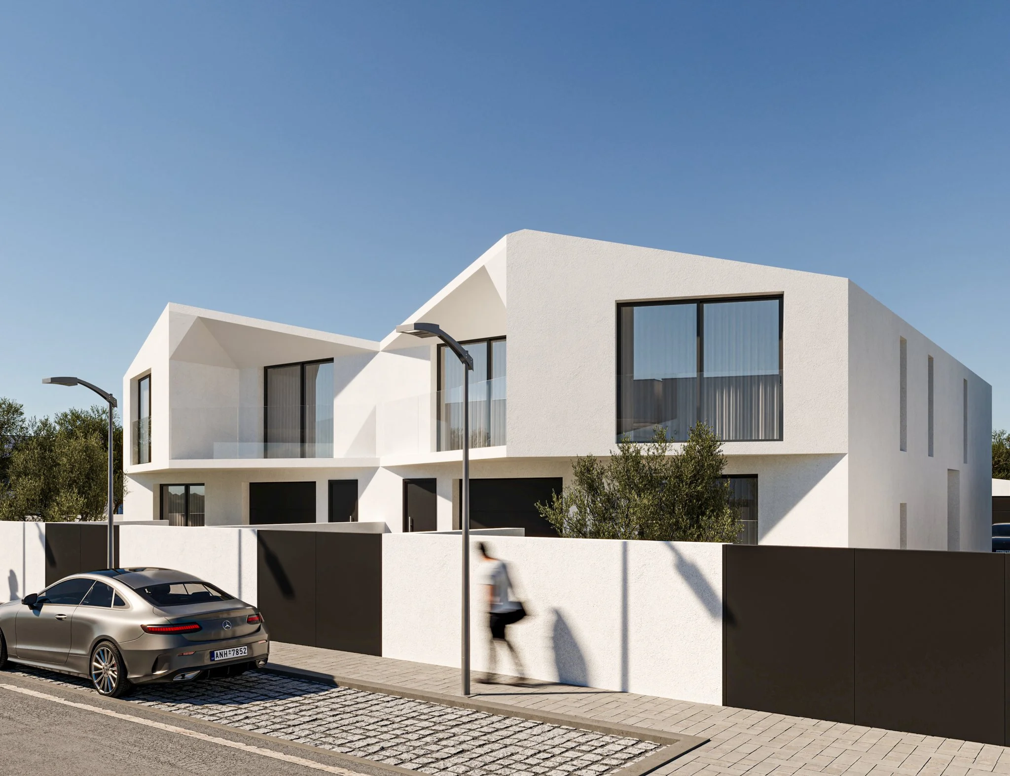 Prédio moderno de fachada branca com janelas grandes, cercado por muro preto e rua com carro e pessoa caminhando.