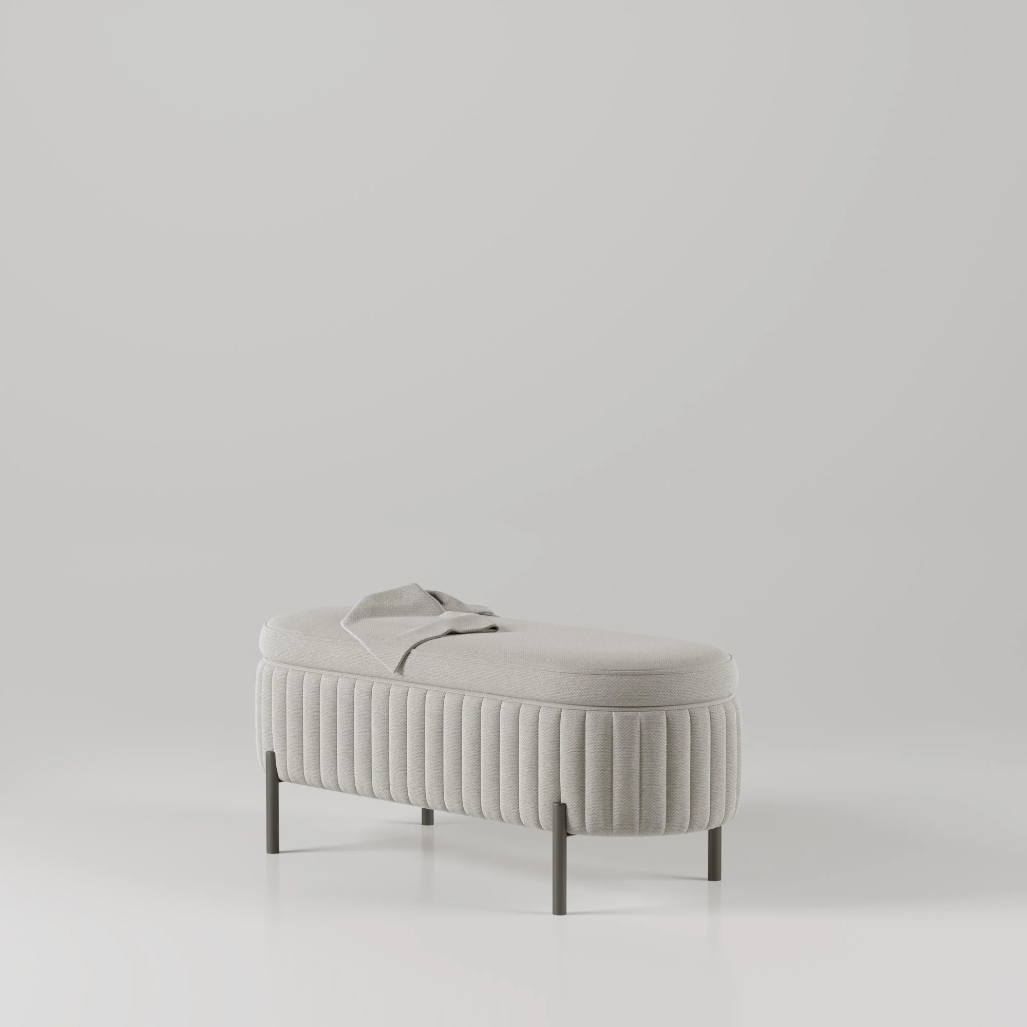 Pufe cinza claro com estrutura de pernas finas pretas, almofada de assento macia, e uma manta cinza colocada sobre ele, em ambiente minimalista.