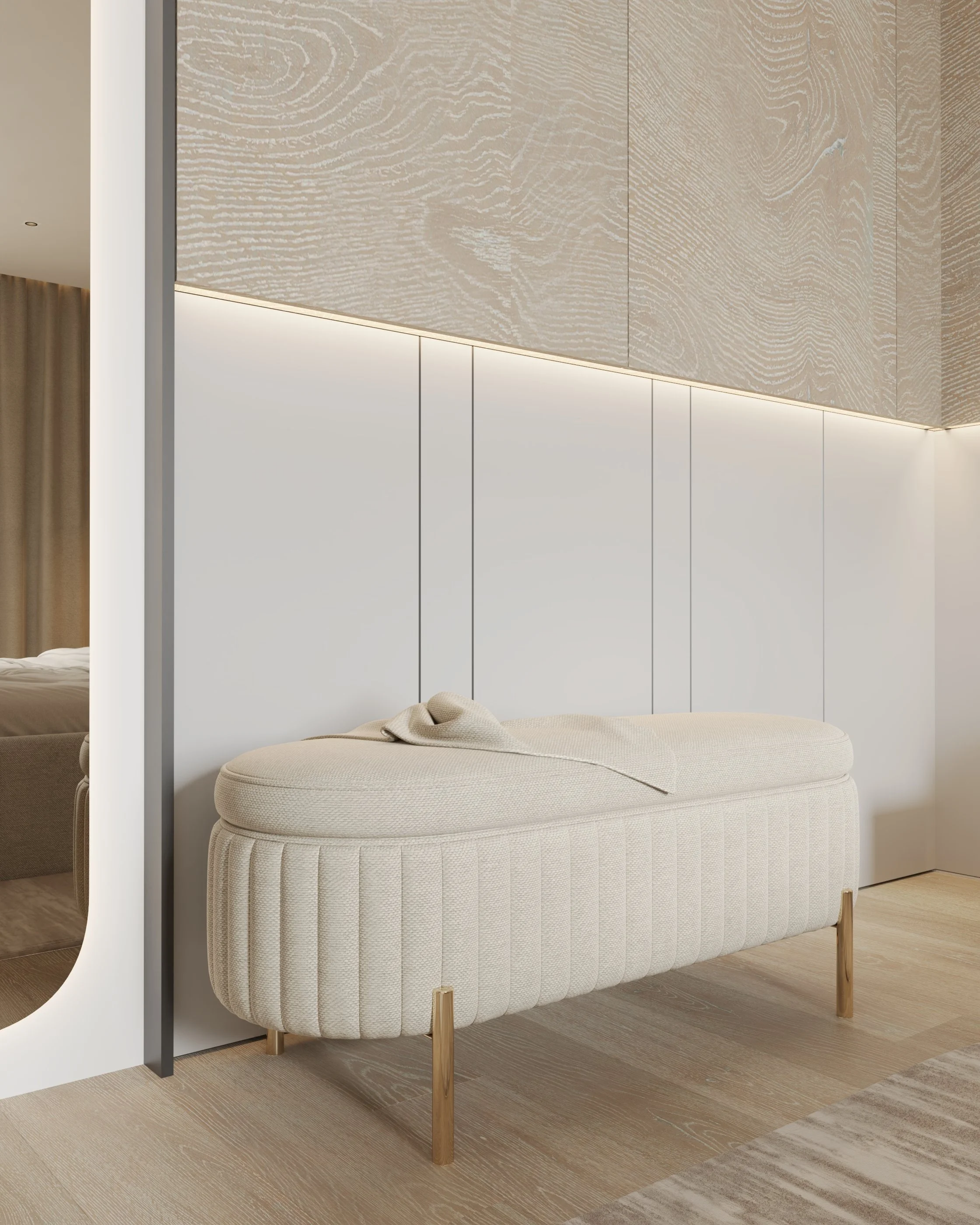 Móvel estofado de cor bege na frente de uma parede branca com iluminação indireta no topo, em um ambiente moderno e minimalista com piso de madeira clara.