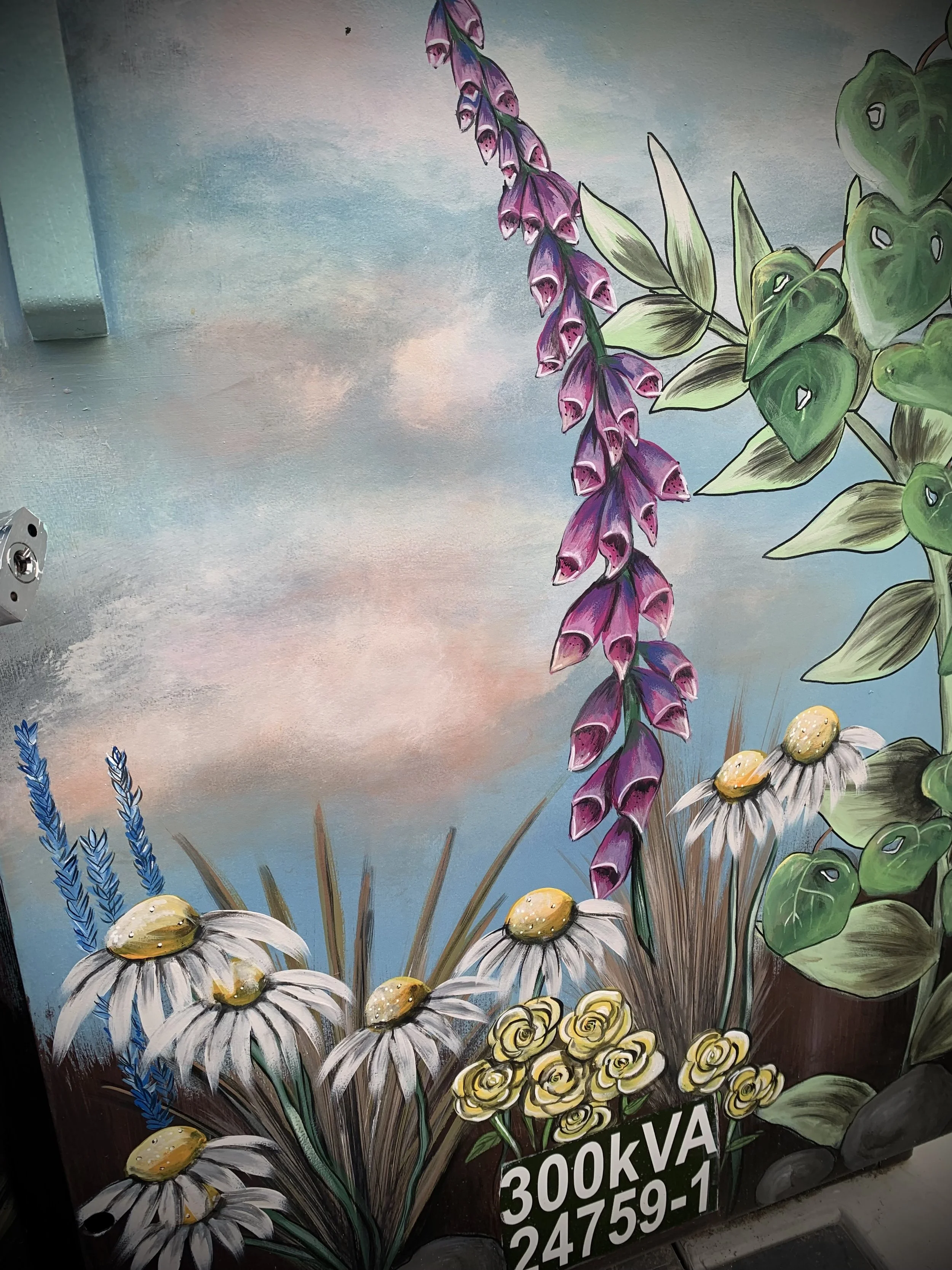 Colorful painted mural of various flowers including purple foxglove, yellow daisies with large centers, small yellow roses, and blue lavender, set against a sky with clouds, with an art identification number at the bottom.
