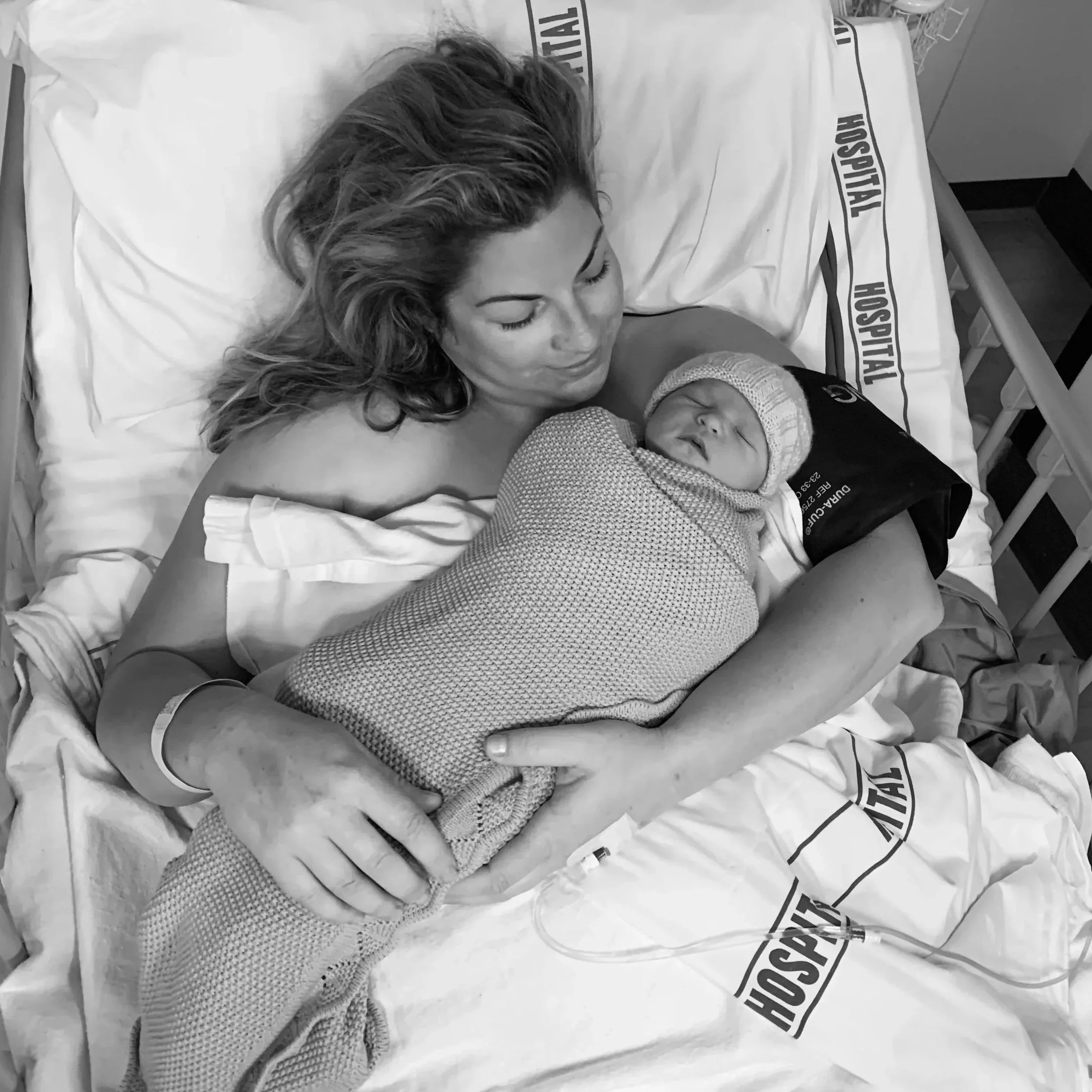 Dannika Tukua in a hospital bed holding her newborn daughter wrapped in a blanket.