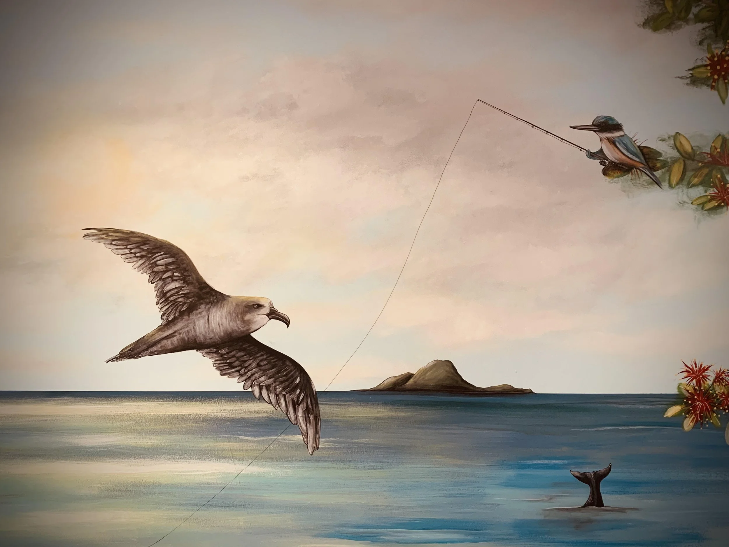 A mural artwork depicting a fishing scene where a large bird, possibly an eagle or hawk, is soaring above a body of water with a fishing line attached to a smaller bird perched on a branch. The smaller bird is holding a fishing rod, and a whale's tai