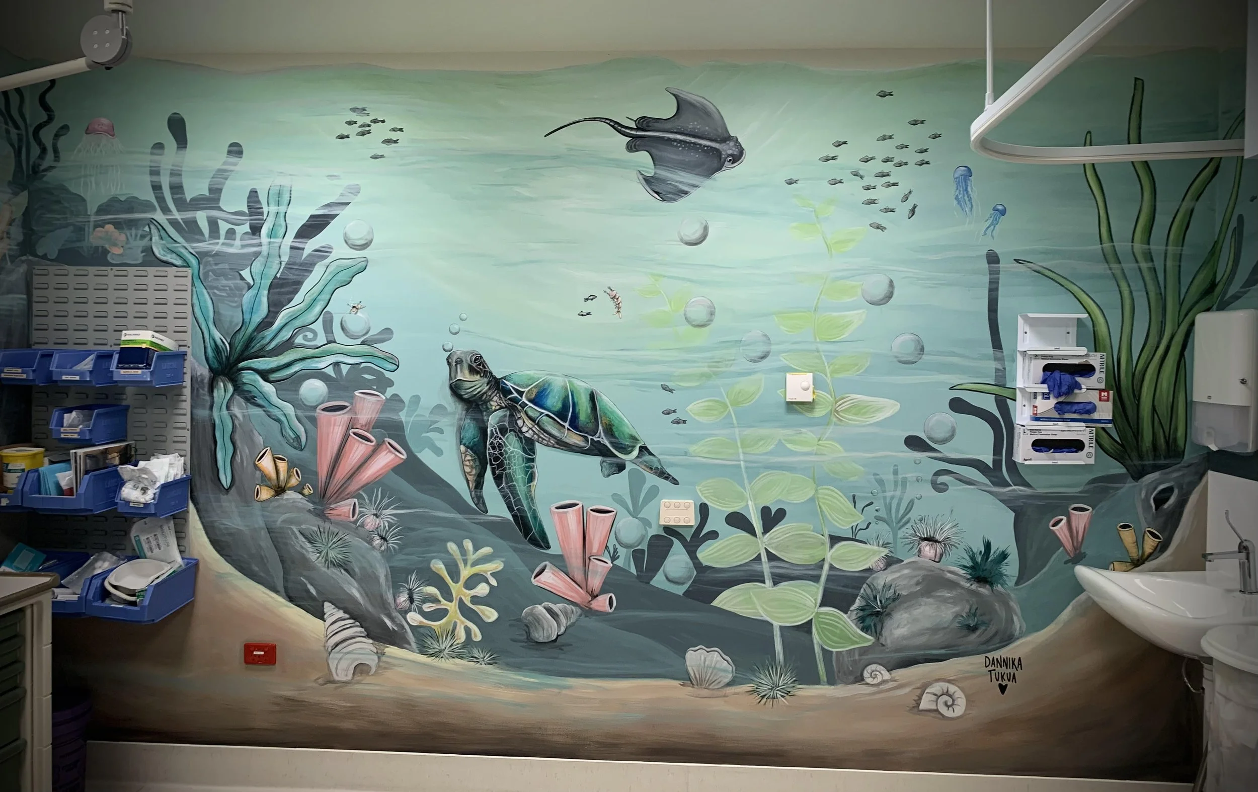 Underwater ocean scene mural with marine life, including a turtle, stingray, jellyfish, various fish, and coral, painted on a wall.