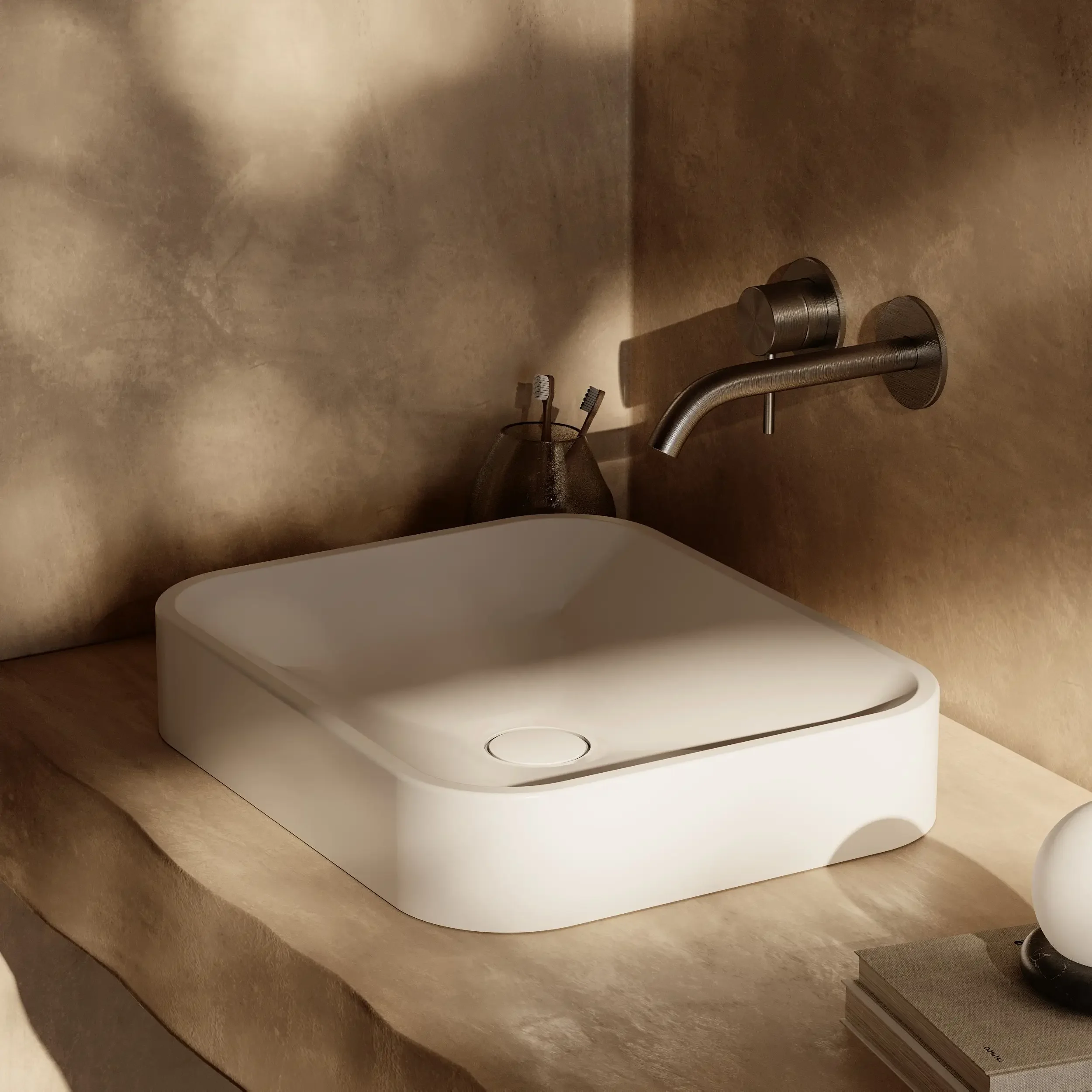 Close-up of metallic bathroom fixtures, including a faucet with a curved spout, a round control knob, and toothbrushes in a holder, set against a beige or light brown wall.