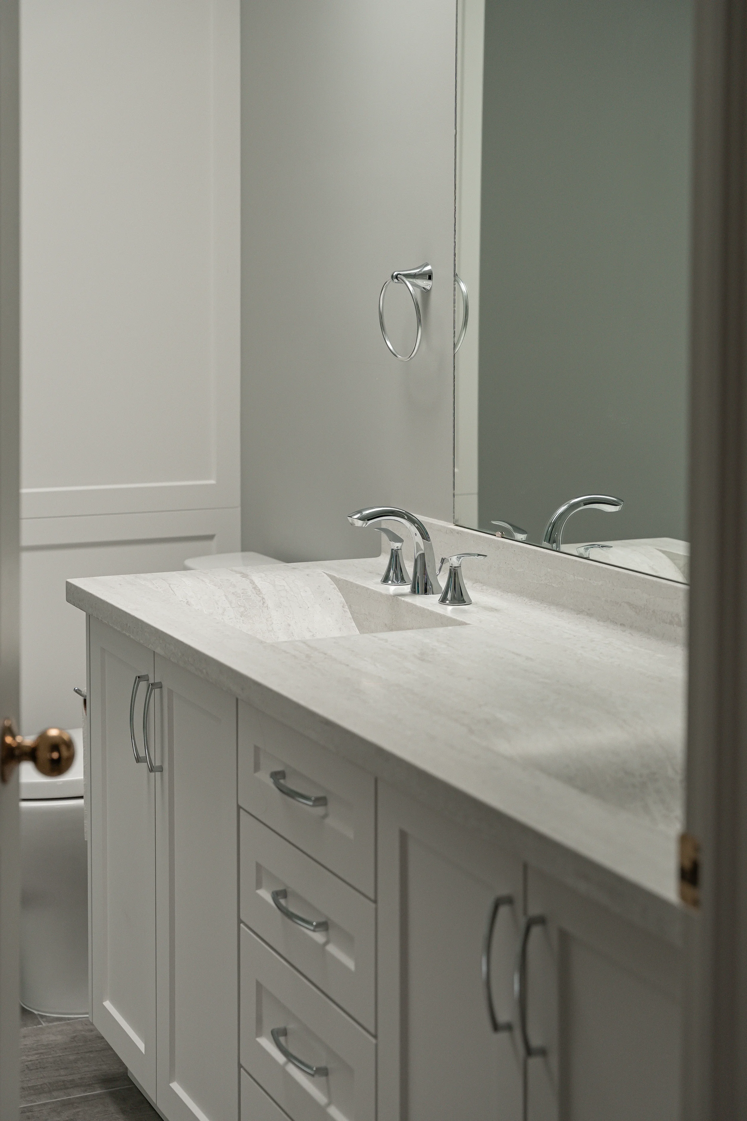 White bathroom vanity with marble countertop, silver faucet, mirror, and cabinet with handles in a bathroom.