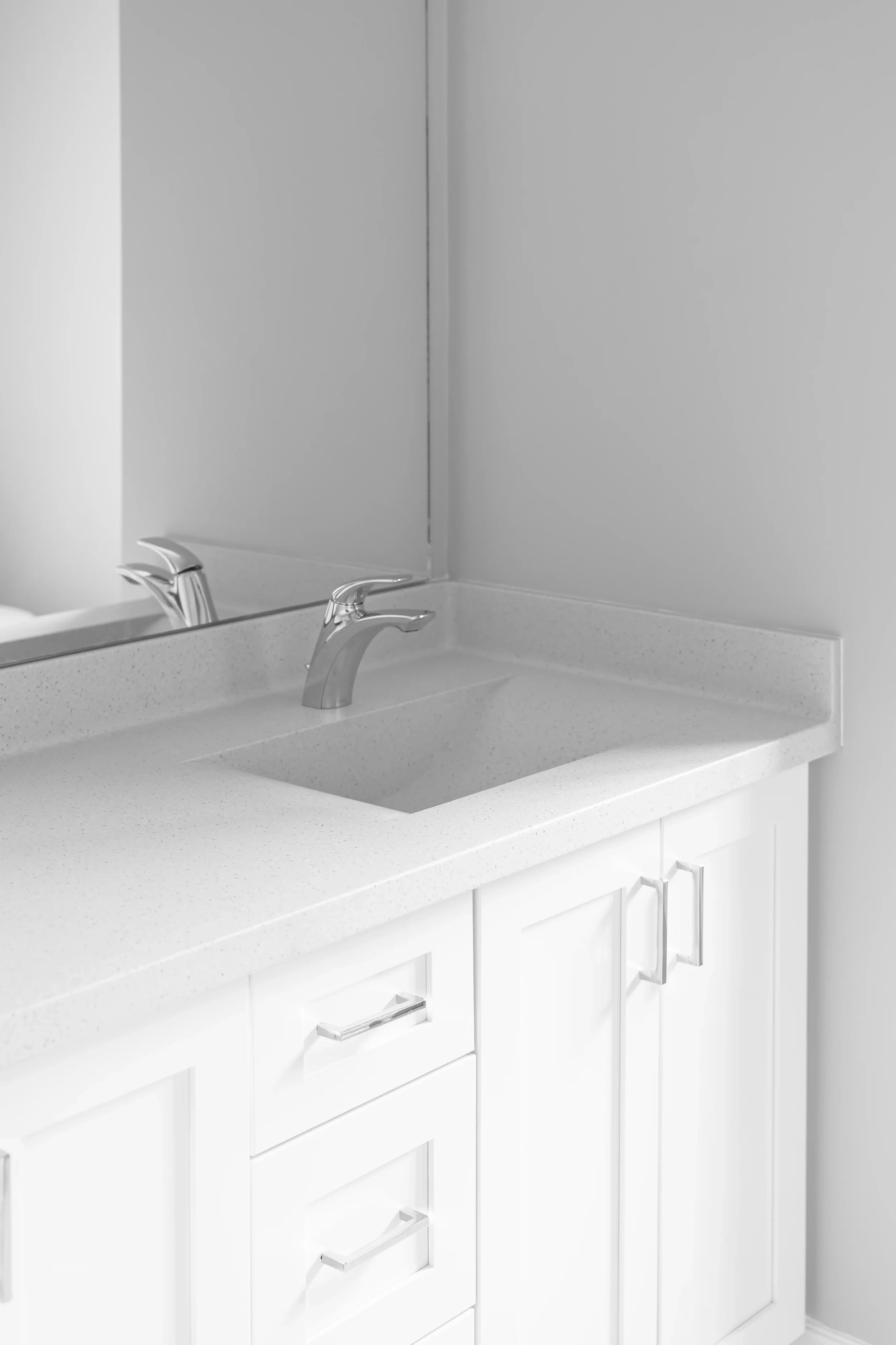 White bathroom vanity with double sinks, two silver faucets, and storage cabinets with silver handles, with a large mirror above.