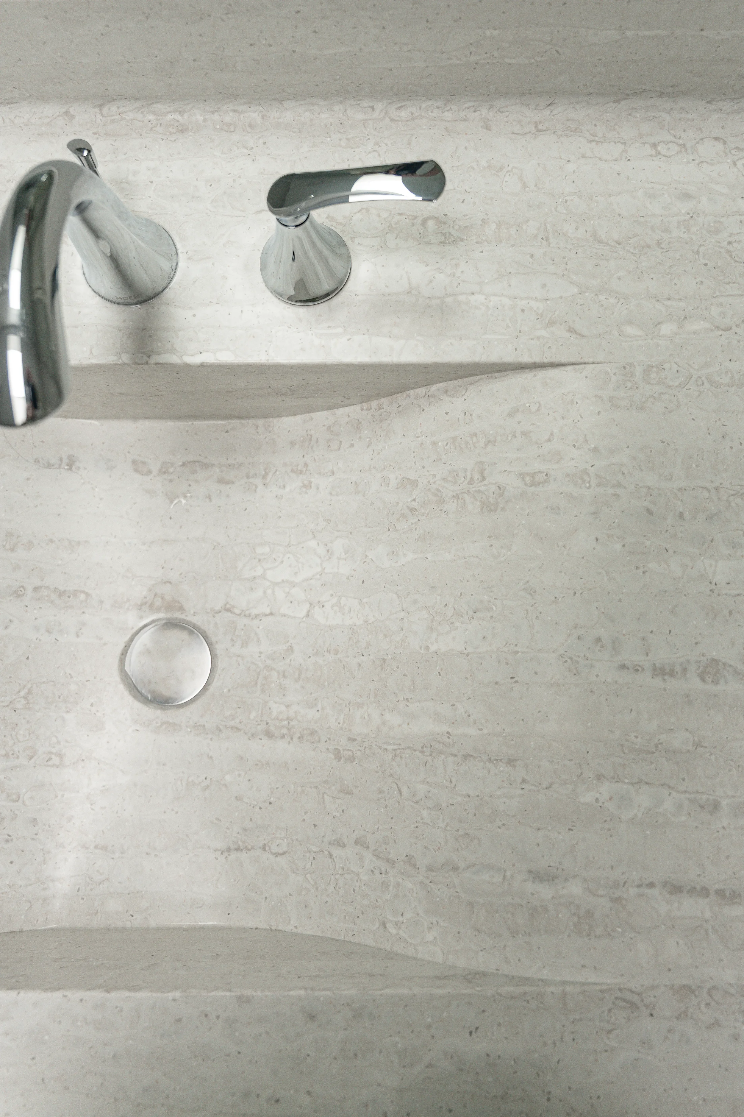 A close-up of a bathroom sink with a shiny chrome faucet and a drain, all mounted on a beige speckled countertop.