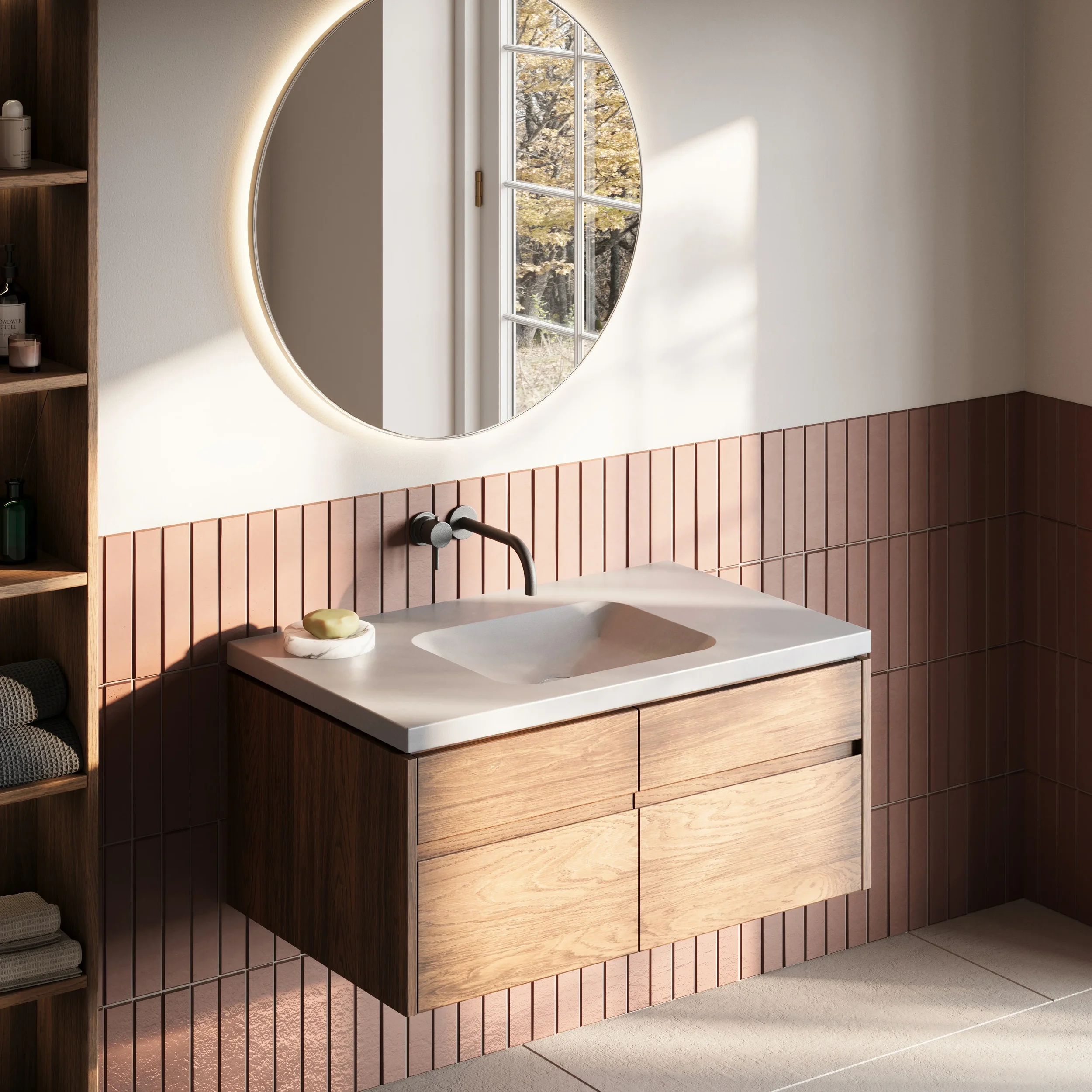 Modern bathroom with a large oval mirror, a white countertop with an integrated sink, dark wood cabinets, pink tiles on the wall, and a window showing trees with autumn foliage.