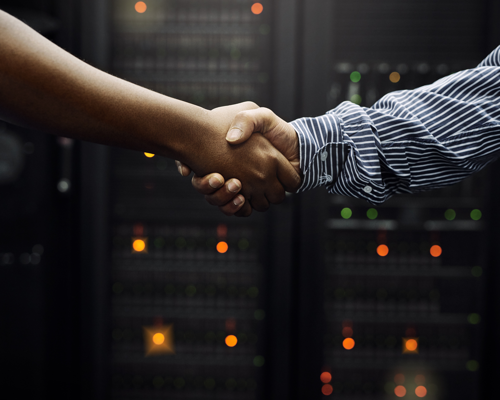 Zwei Personen schütteln sich die Hand vor einem Serverraum mit leuchtenden Geräten.