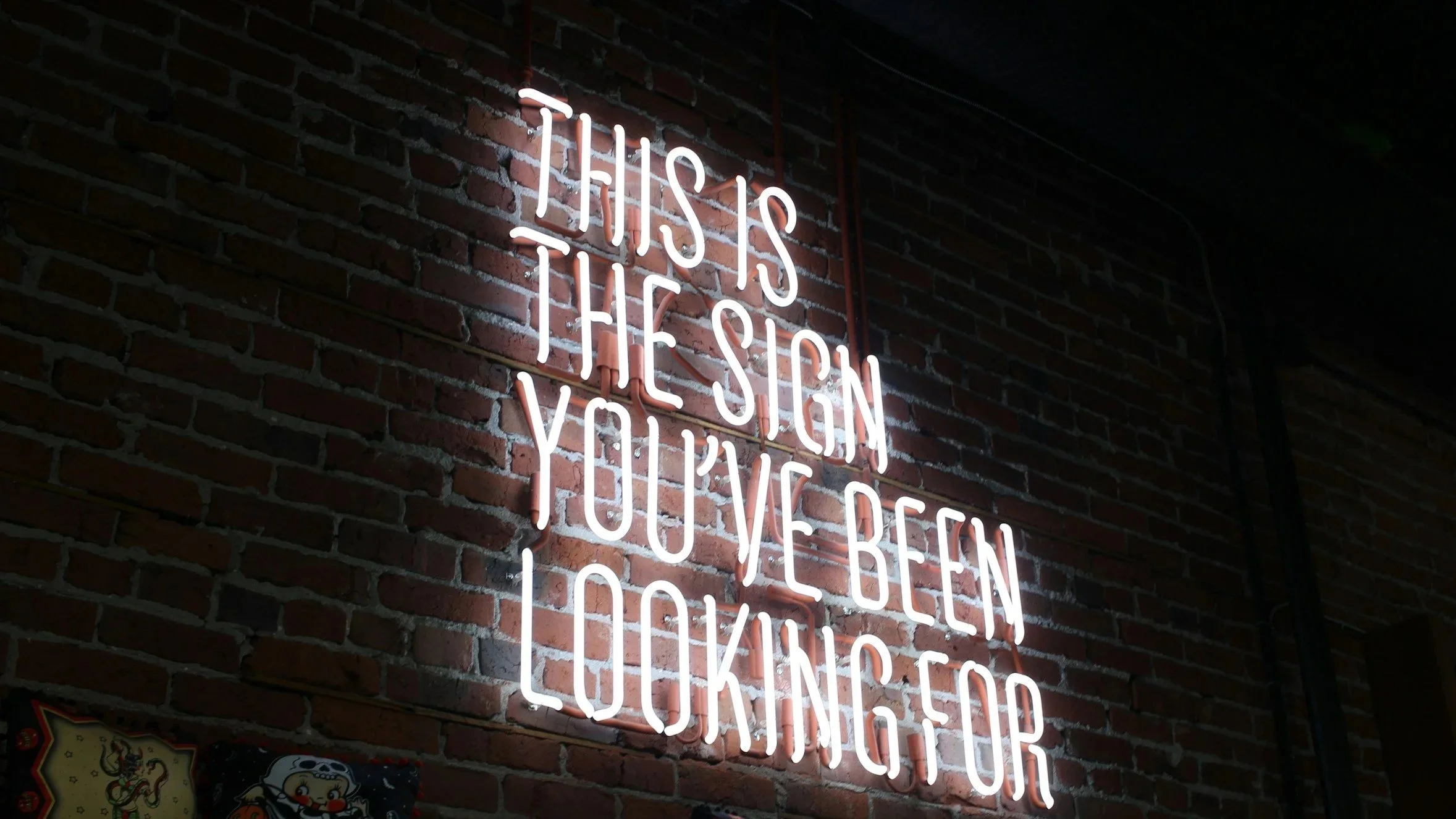 Leuchtendes Neon-Schild mit der Aufschrift "This is the sign you've been looking for" an einer Ziegelmauer.