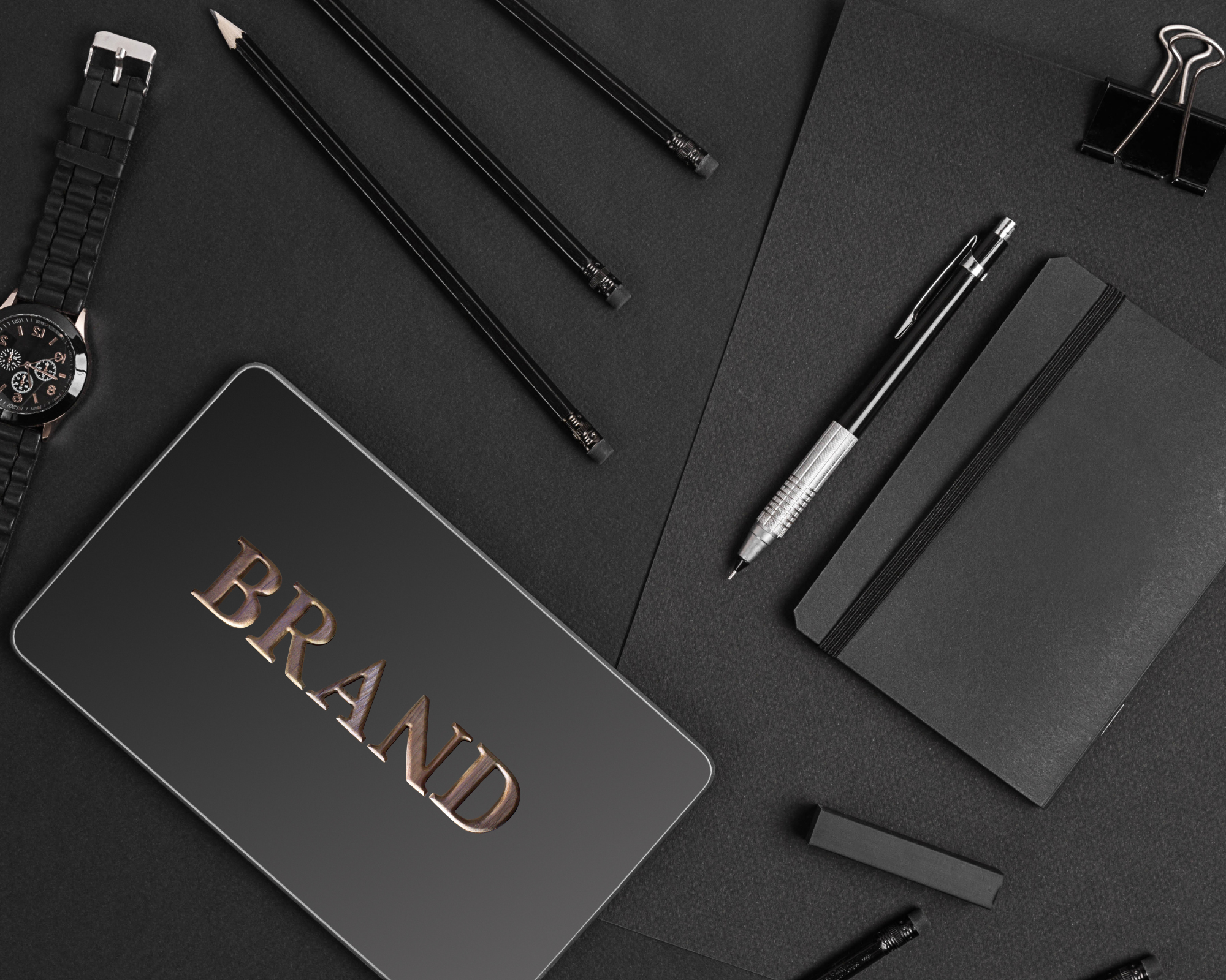 Schwarze Schreibwaren, inklusive Notizbuch, Kugelschreiber, Marker, Uhren, und eine Tafel mit der Aufschrift 'BRAND' auf schwarzem Hintergrund