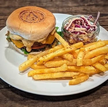 A cheeseburger with lettuce, tomato, cheese, and a beef patty, served with French fries and a side of coleslaw on a white plate.