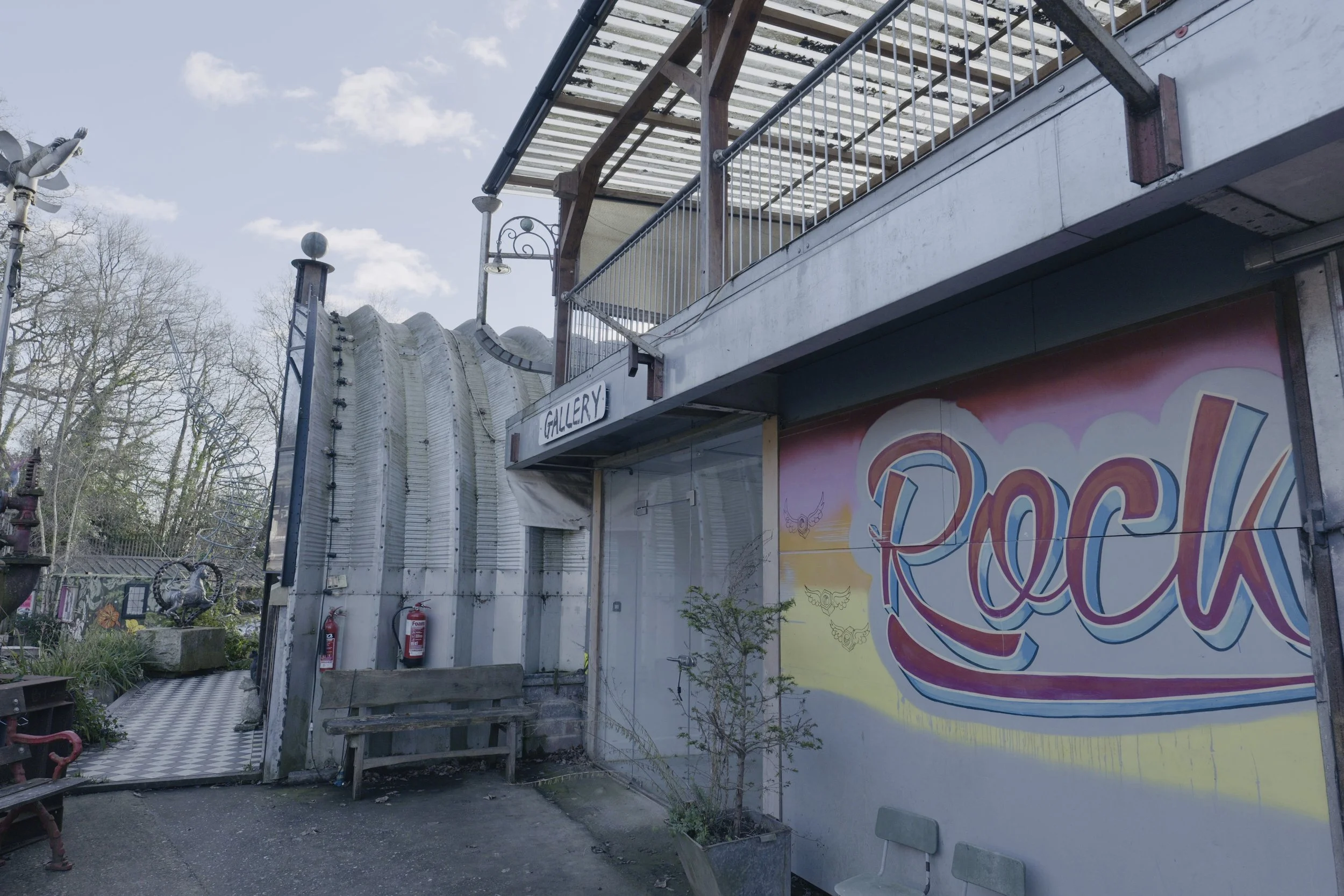 Exterior of a building with a colorful mural reading 'Rock', a painted sign that says 'Gallery', and fire extinguishers mounted on the wall.