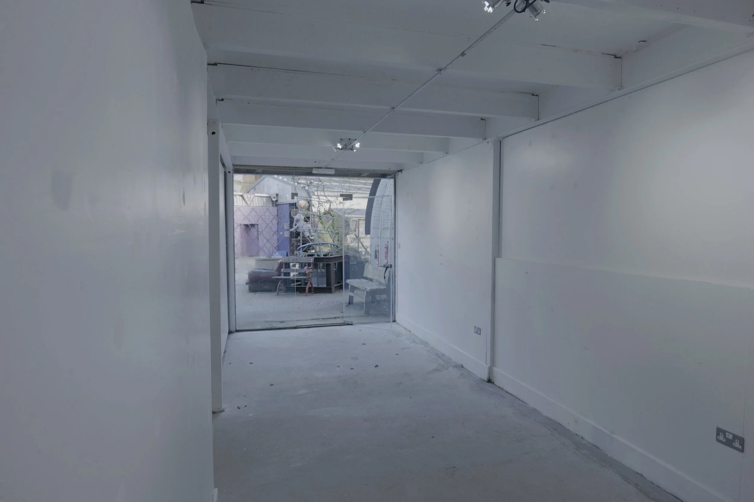 Empty interior corridor leading to a glass door with an outdoor area visible through the door, containing furniture and equipment.