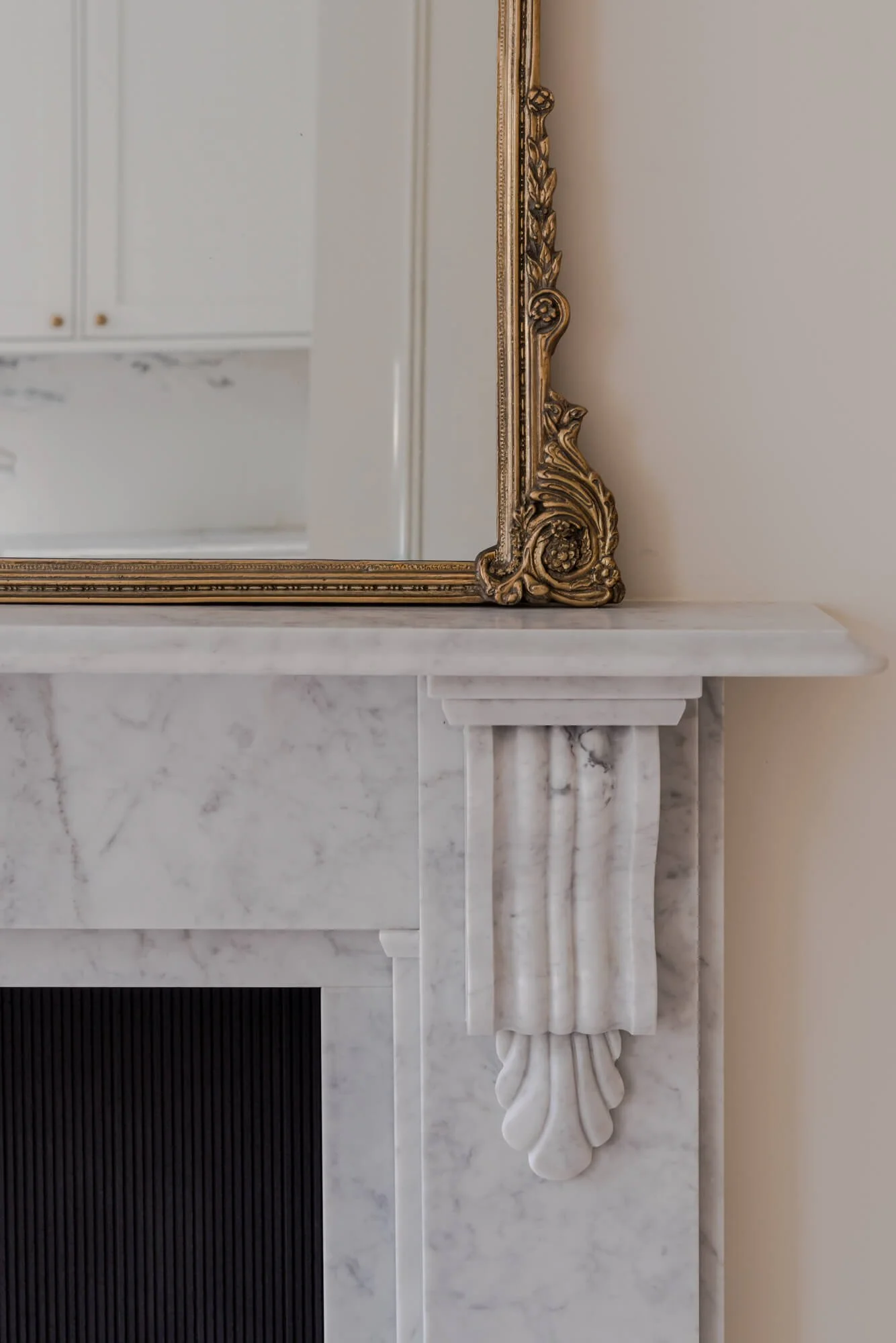 Close-up of a white marble fireplace with decorative corbel and a gold-framed mirror on top of the mantel.