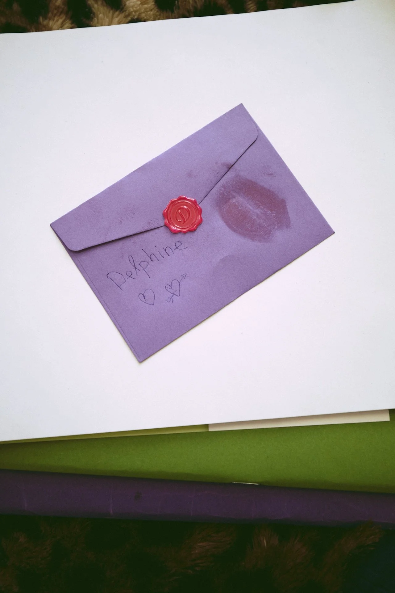 Purple envelope with a red wax seal and handwritten note that says 'Delphine' with hearts and lips