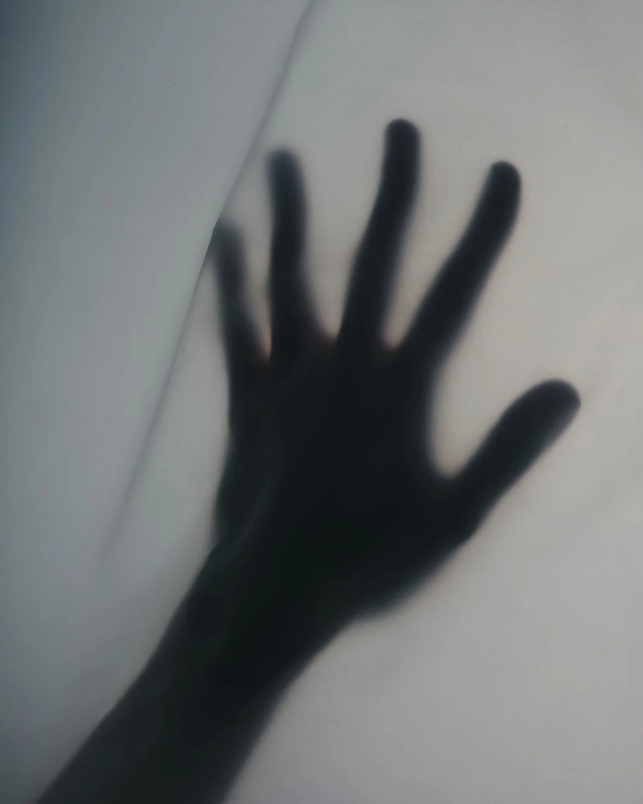 Shadowed silhouette of a hand with fingers splayed out, cast against a light surface, creating a blurred and abstract appearance.