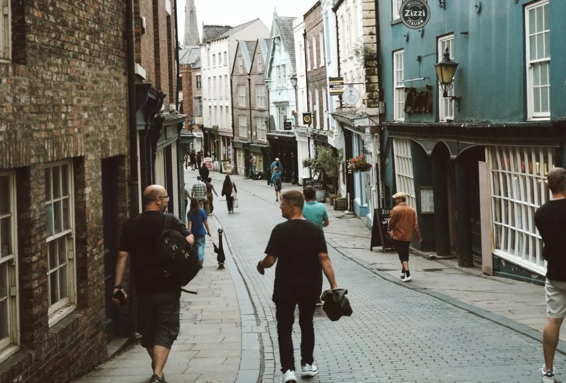 People walking on a narrow, curved street lined with colorful buildings, some with storefronts and signs.