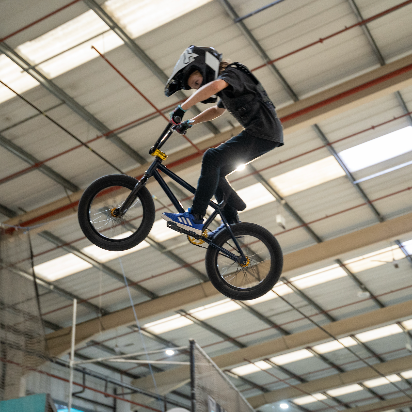 Person performing a BMX stunt indoors with a helmet and black clothing.