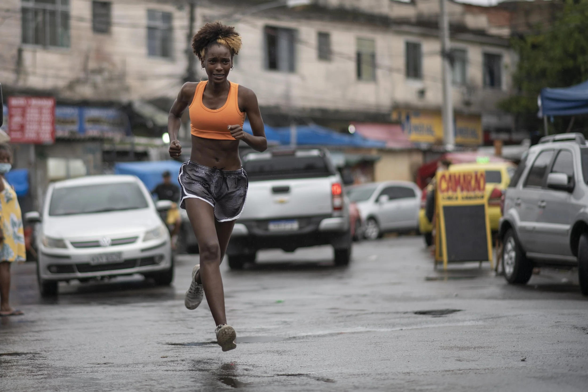A woman running on a wet city street with parked cars and buildings in the background.