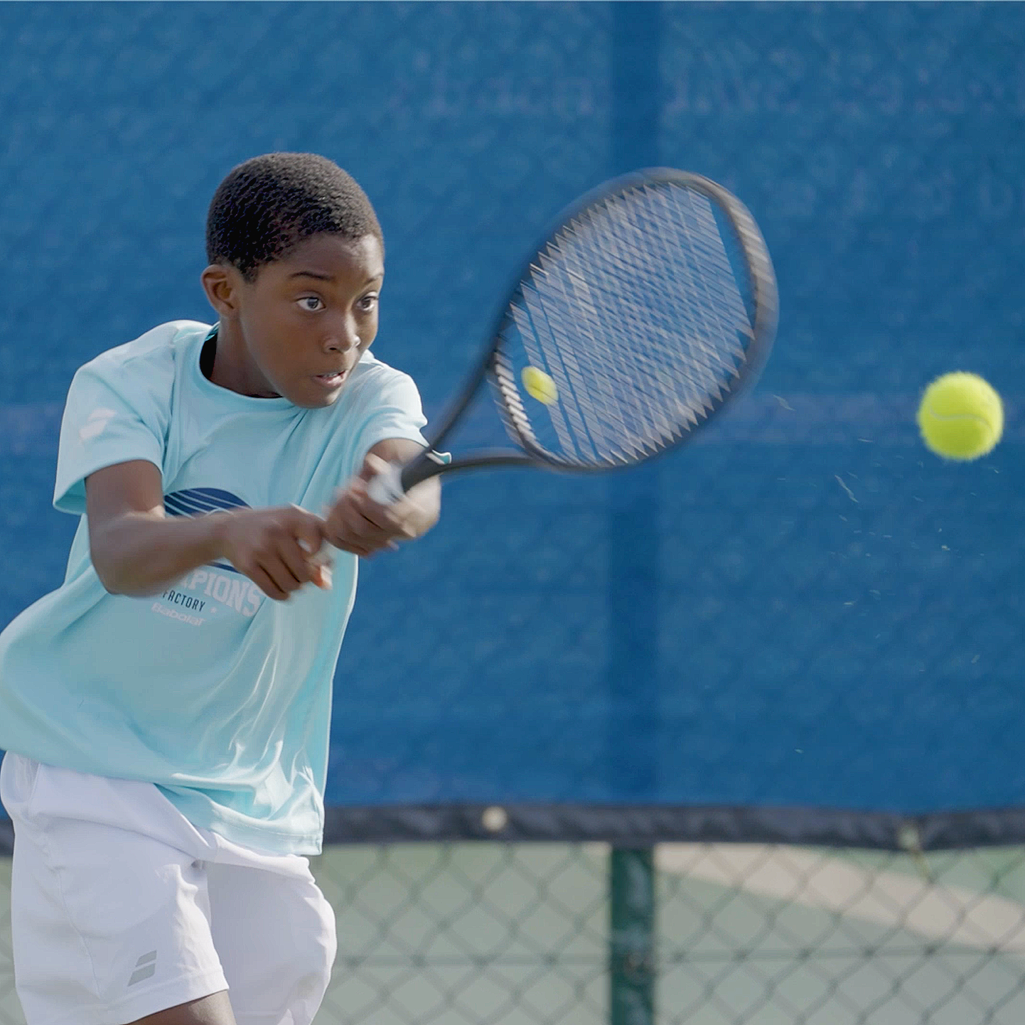 A young boy playing tennis on a court, hitting a tennis ball with a racket.
