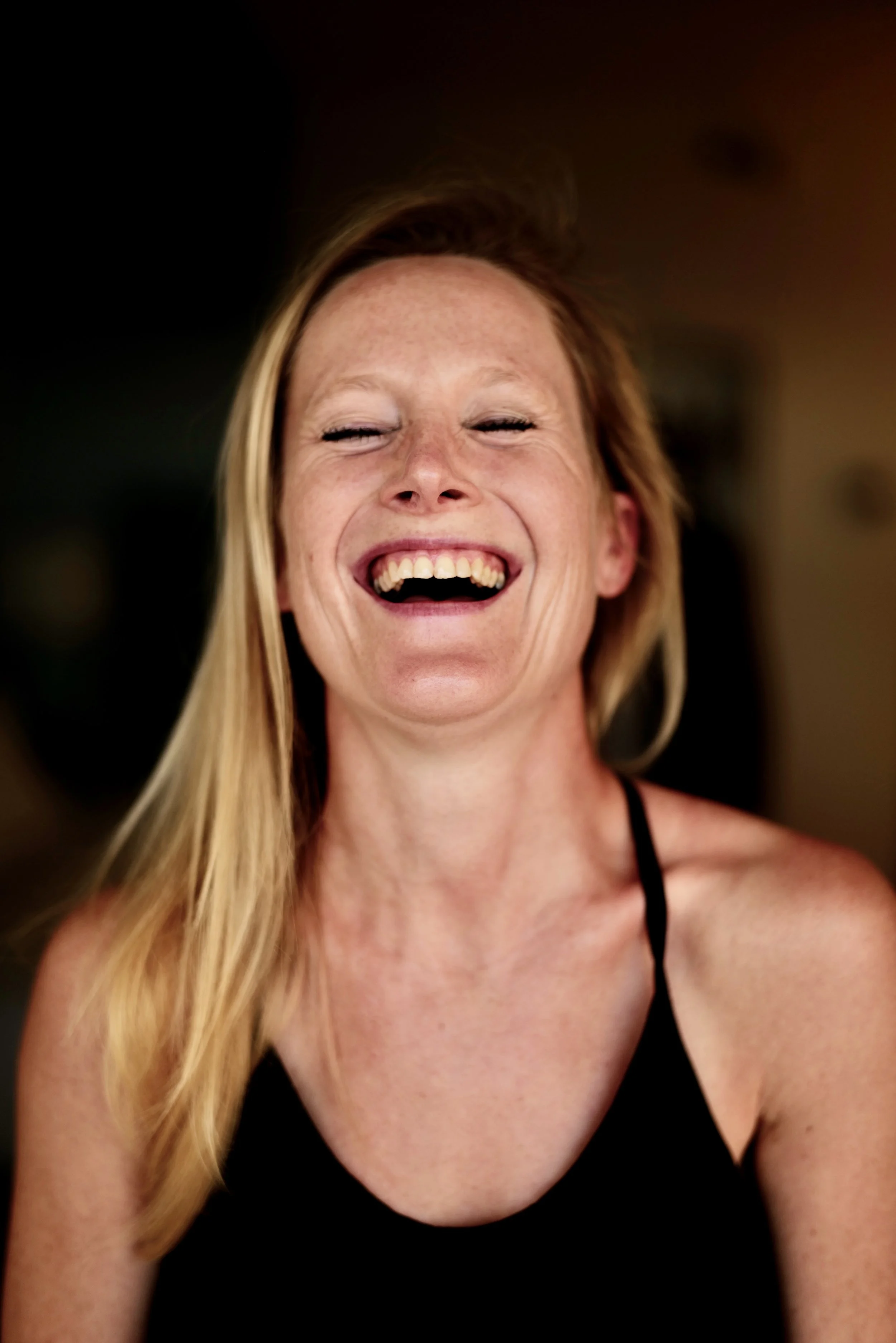 Founder, female director with long blonde hair laughing with her eyes closed, wearing a black tank top.