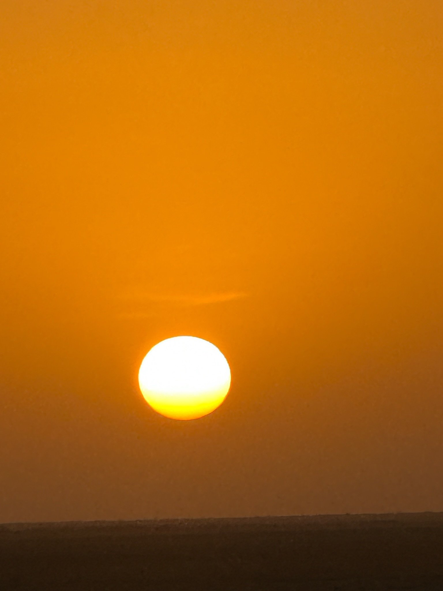 Sunset over the ocean with a clear orange sky.