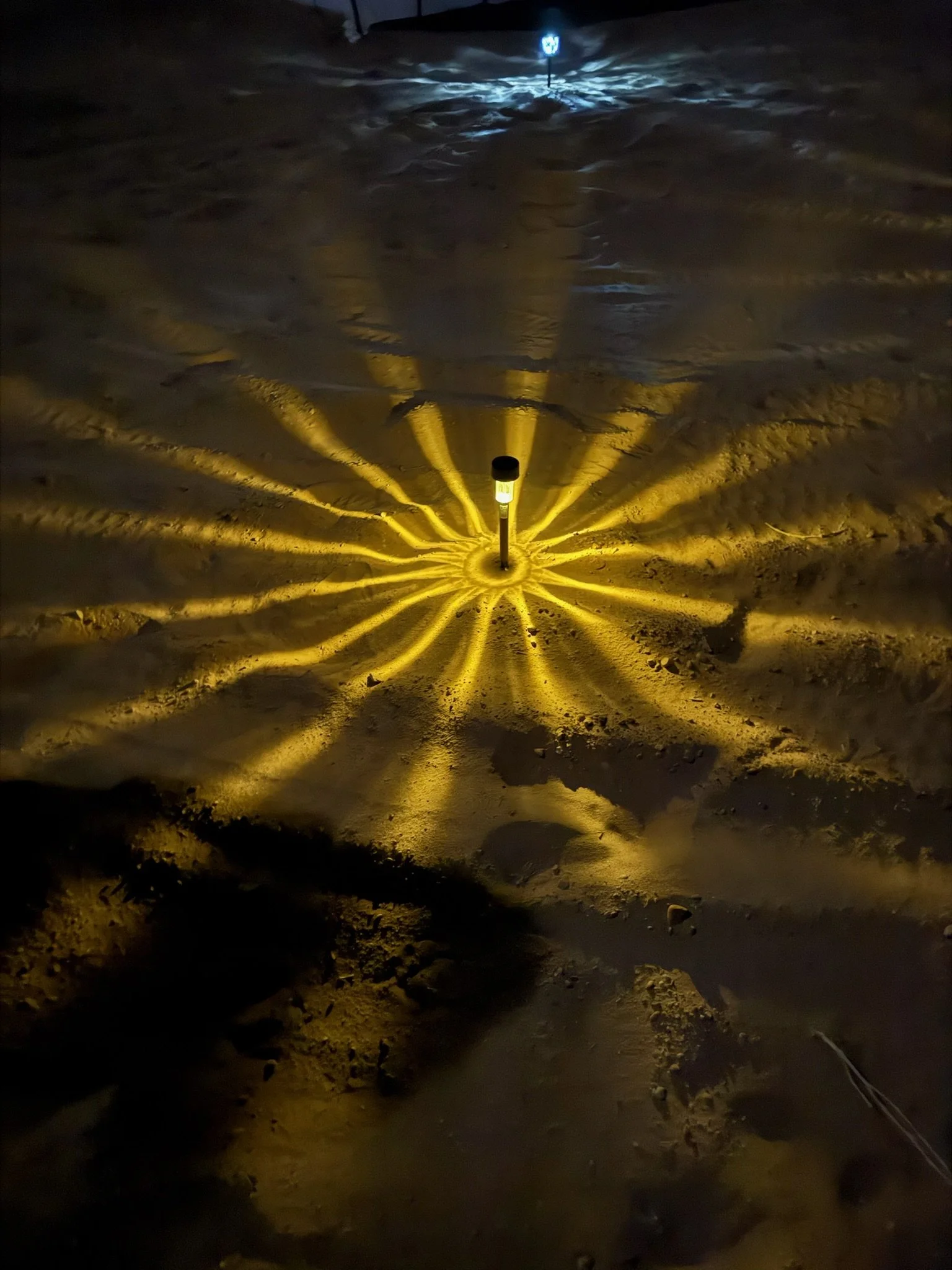 A snow-covered ground at night with a series of yellow lights in a circular pattern and a small blue light in the distance.