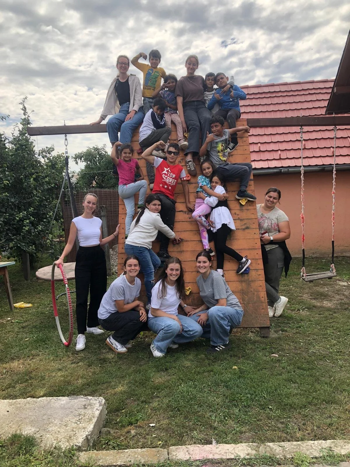 Gruppe von jungen Menschen und Kindern, die eine Kletterwand im Garten erklimmen.