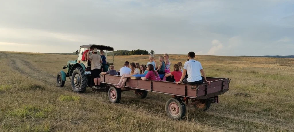Gruppe von Kindern sitzt auf einer Kutschfahrt in einer offenen ländlichen Landschaft bei Sonnenuntergang.