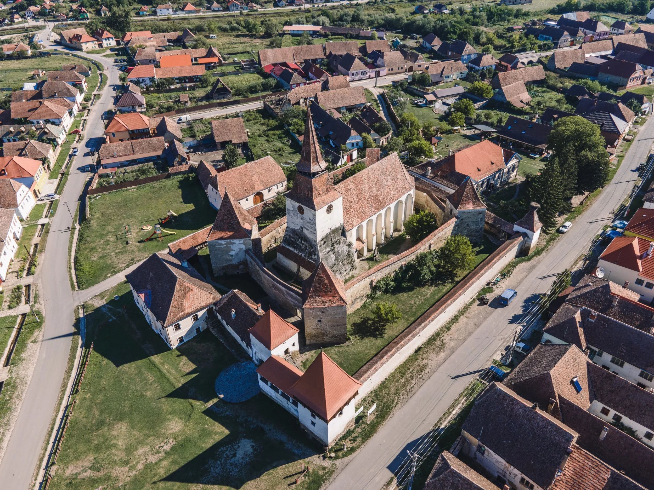 Luftaufnahme eines alten Schlosses oder einer Burgruine in einem kleinen Dorf, umgeben von Wohnhäusern mit roten Dächern, umgeben von Straßen und Bäumen.