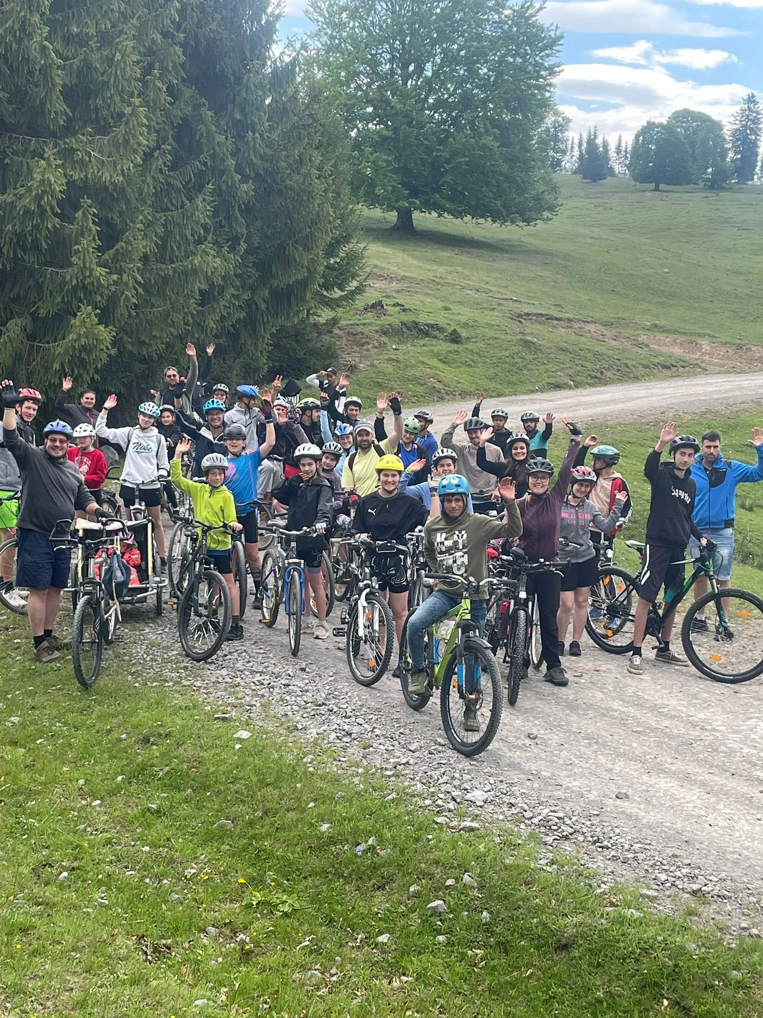 viele Kinder und Jugendliche auf Fahrrädern haben in einer Kurve angehalten, im Hintergrund Bäume und eine Wiese