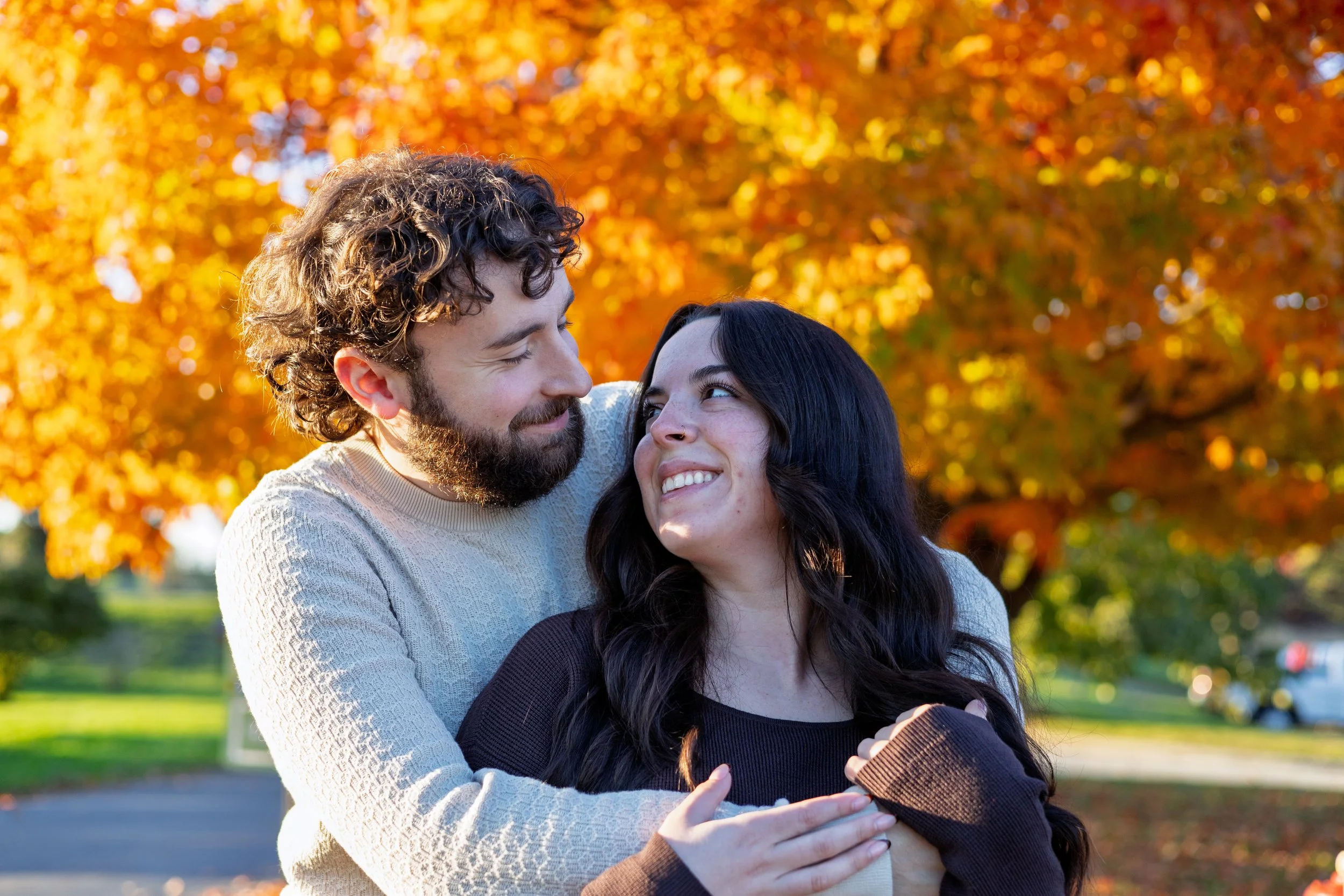 A happy couple embracing outdoors during autumn, with colorful fall leaves in the background.