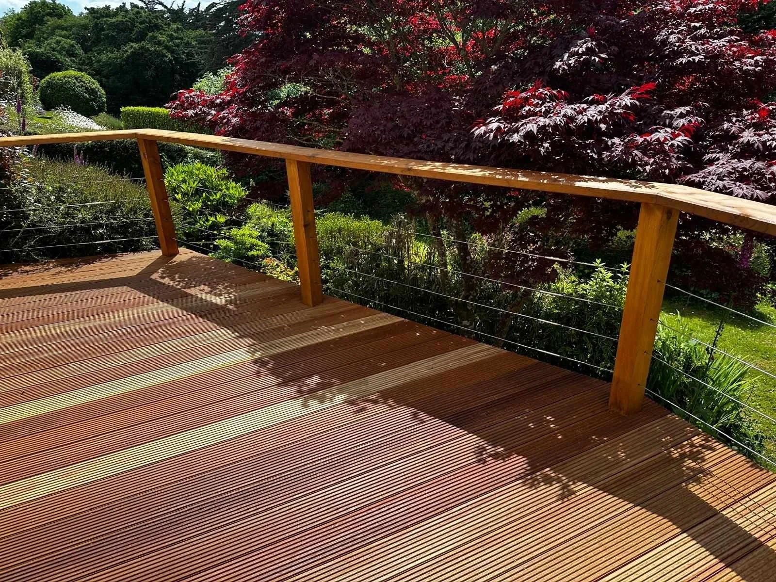 Wooden deck with a railing overlooking a garden with trees and bushes.