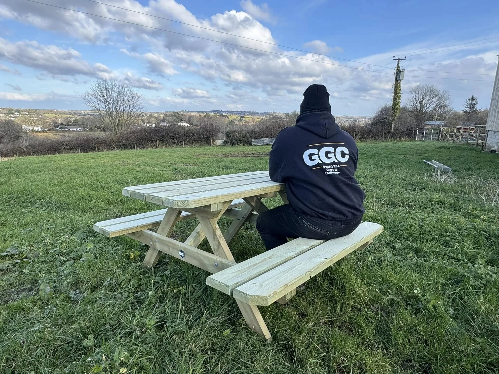 Kristen boss man wearing a black hoodie with GGC logo sat on bespoke wooden picnic bench.