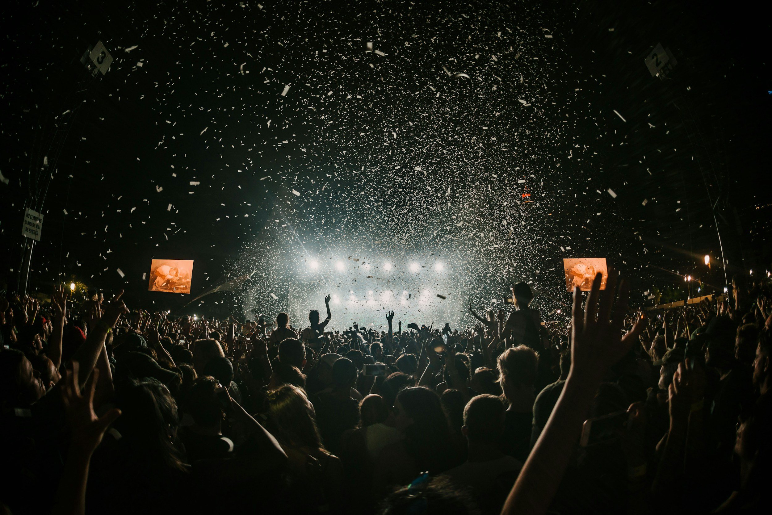Crowd at a concert with confetti falling and bright stage lights.