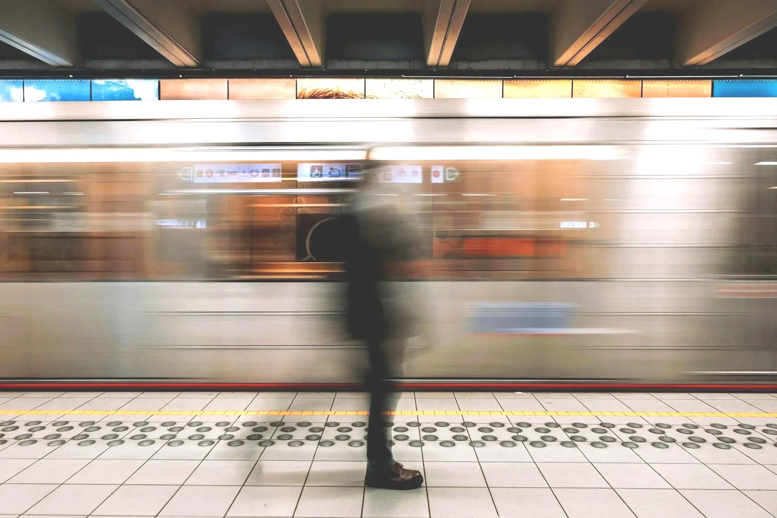 A person standing on a subway platform as a train passes by at high speed, creating a blurred motion effect.