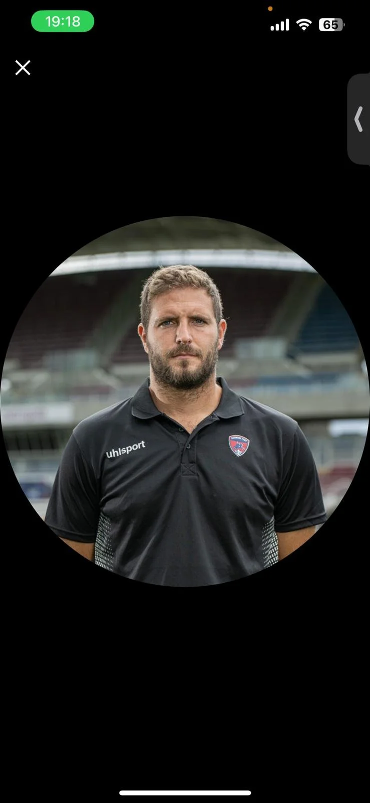 Un homme avec une barbe porte un t-shirt noir de sport dans un stade vide.
