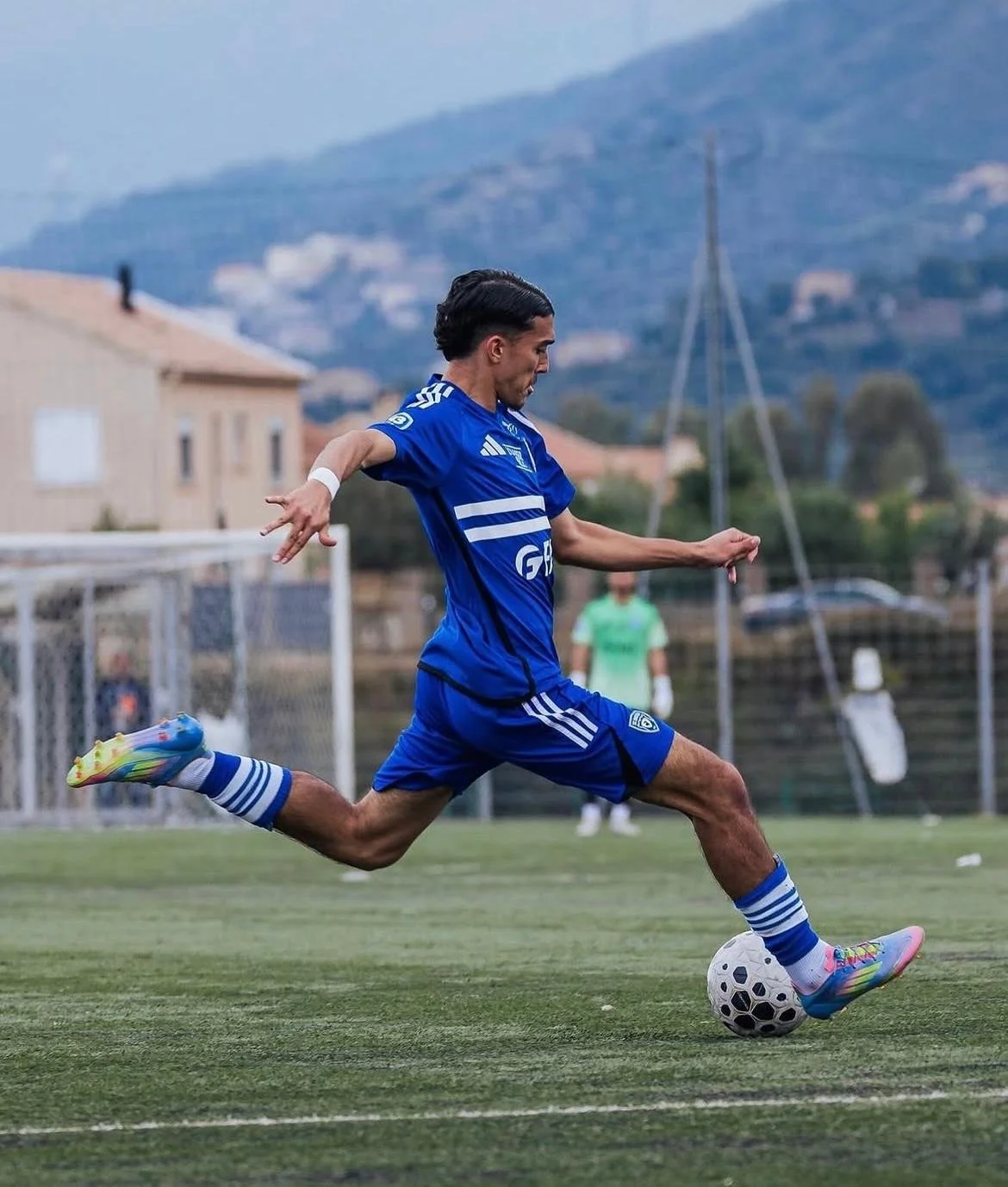 Joueur de football en action, portant un uniforme bleu, en train de kick le ballon sur le terrain.