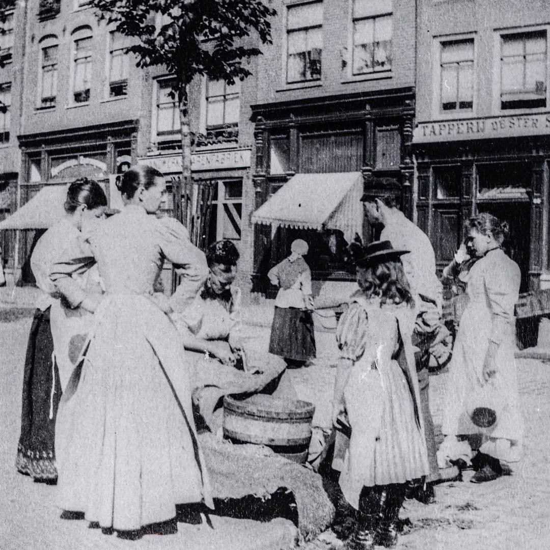 1910 &amp; Now: in this photo you see the houses of Elandsgracht 92-82, close to the entrance of Hazenstraat. In the center of the photo, a fish seller is busy cleaning some fish while a group of ladies gather around her. #thenandnowamsterdam